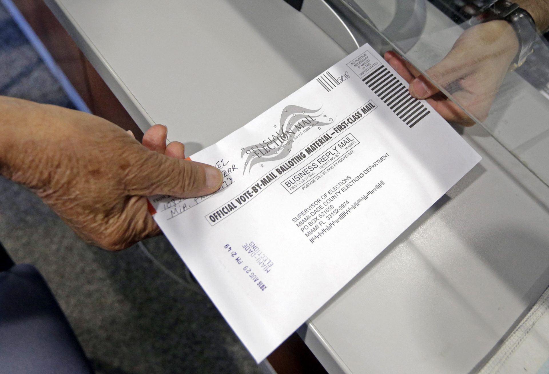 FILE PHOTO: A voter hands his absentee ballot to a Miami-Dade County elections official.