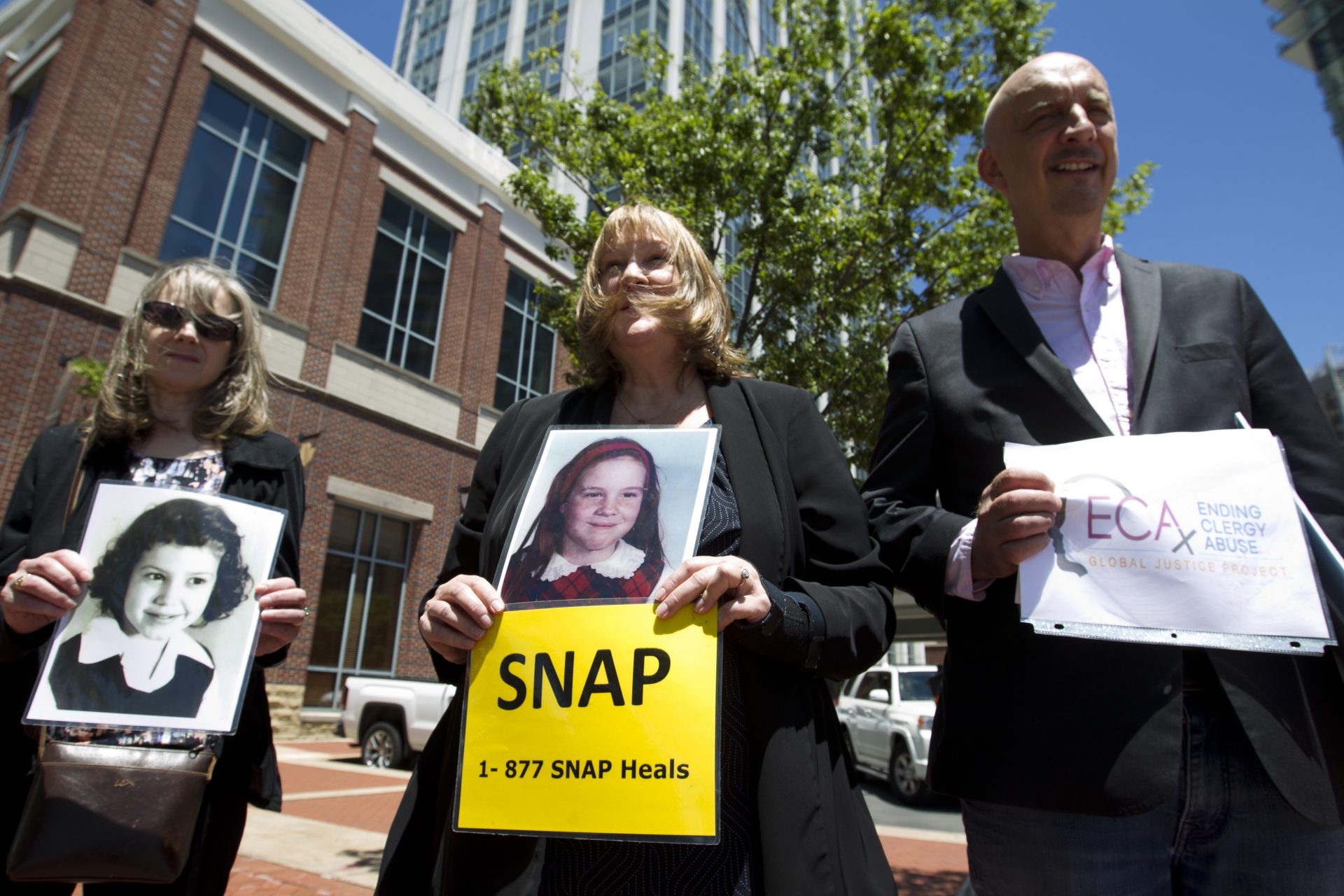 Becky Ianni, center, a victim of priest abuse, holds a picture of her younger self as she joins other demonstrators outside the venue where the United States Conference of Catholic Bishops 2019 Spring meetings are being held in Baltimore, Tuesday, June 11, 2019. Ianni says she was 8 years old when the priest of her family parish began to abuse her.