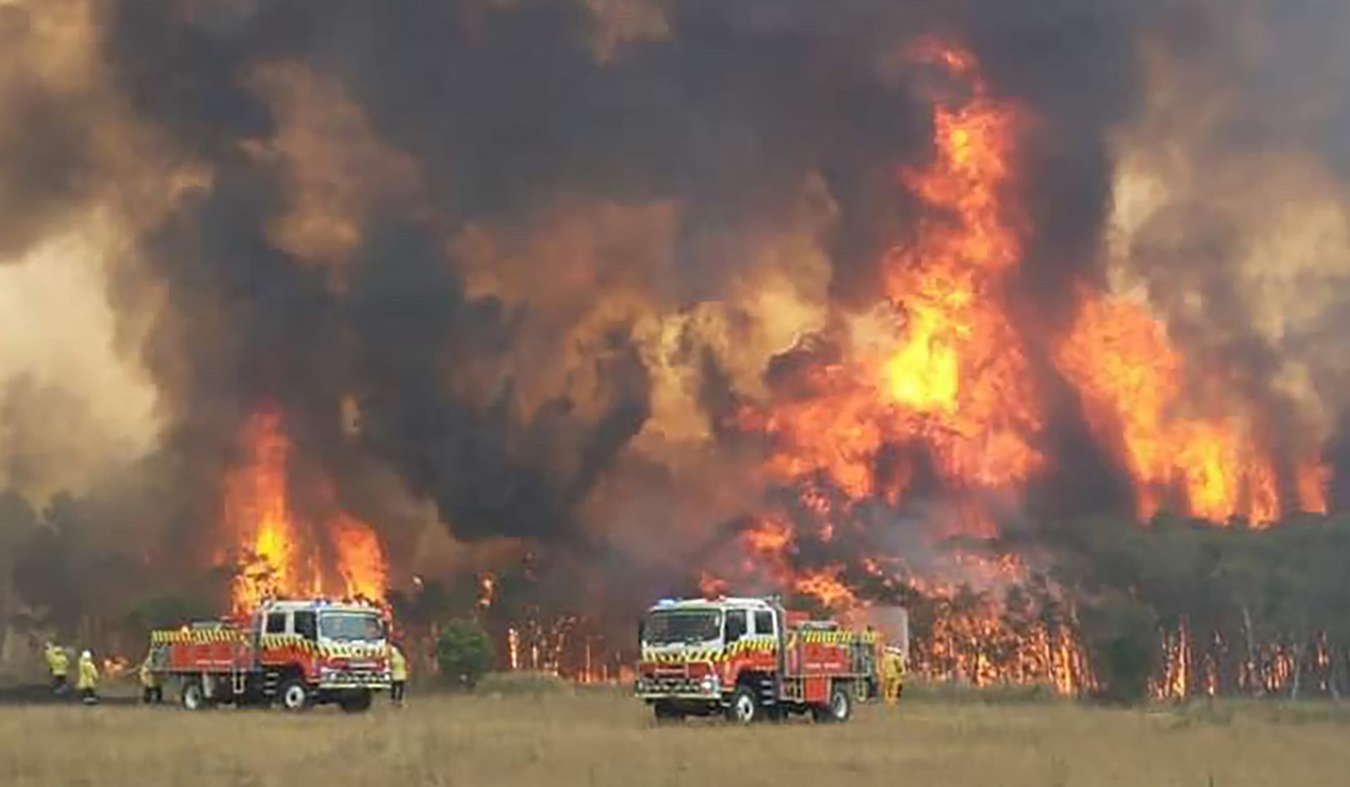 In this image dated Dec. 30, 2019, and provided by NSW Rural Fire Service via their twitter account, firefighters are seen as they try to protect homes around Charmhaven, New South Wales. Wildfires burning across Australia's two most-populous states Tuesday trapped residents of a seaside town in apocalyptic conditions, destroyed many properties and caused fatalities.