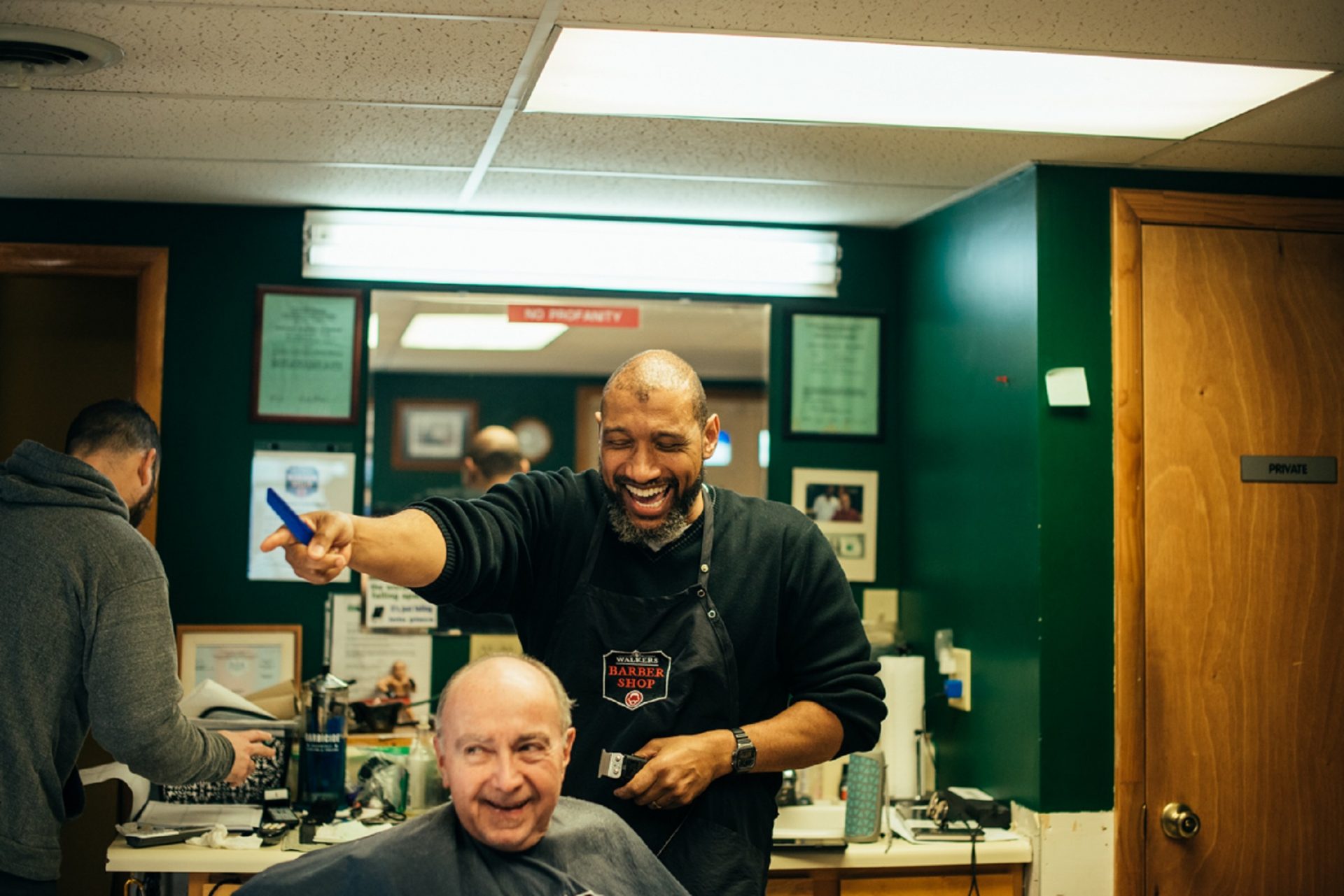 Lance Walker laughs while giving customer Tom Buckus a haircut.