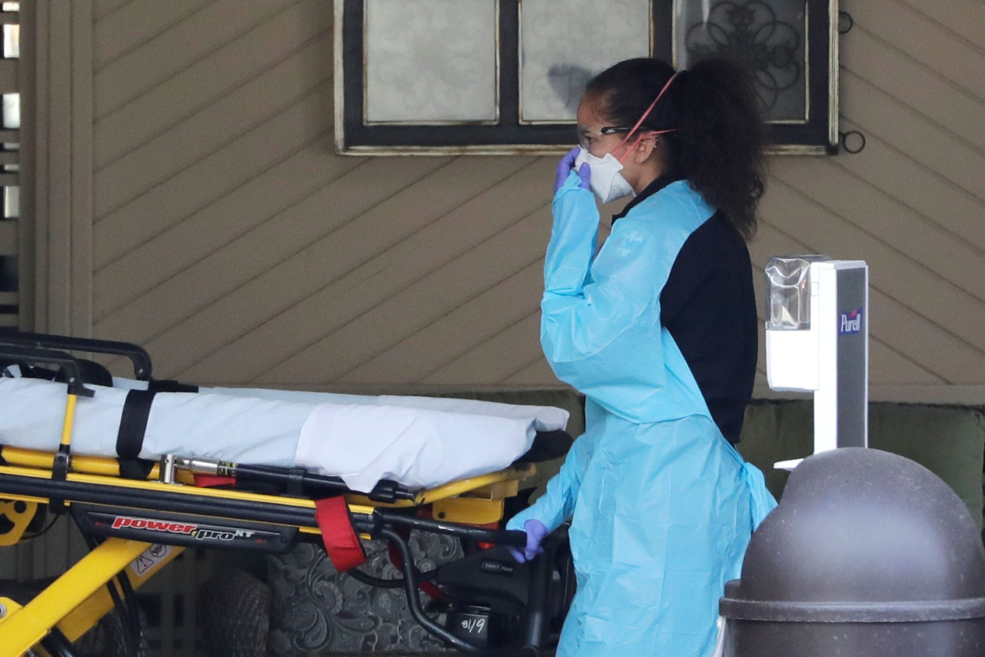 An ambulance worker adjusts her protective mask as she wheels a stretcher into a nursing facility where more than 50 people are sick and being tested for the COVID-19 virus, Saturday, Feb. 29, 2020, in Kirkland, Wash. Health officials reported two cases of COVID-19 virus connected to the Life Care Center of Kirkland. One is a Life Care worker, a woman in her 40s who is in satisfactory condition at a hospital, and the other is a woman in her 70s and a resident at Life Care who is hospitalized in serious condition. Neither have traveled out of the country.