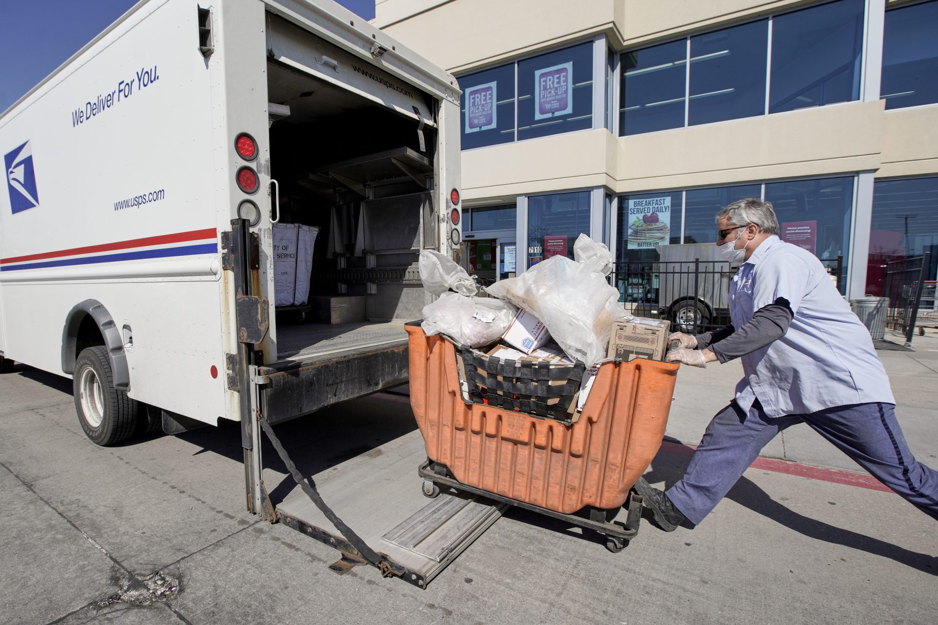 A postal worker wears protective gear against the coronavirus as he collects articles of mail outside a supermarket in Omaha, Neb., Friday, April 10, 2020.