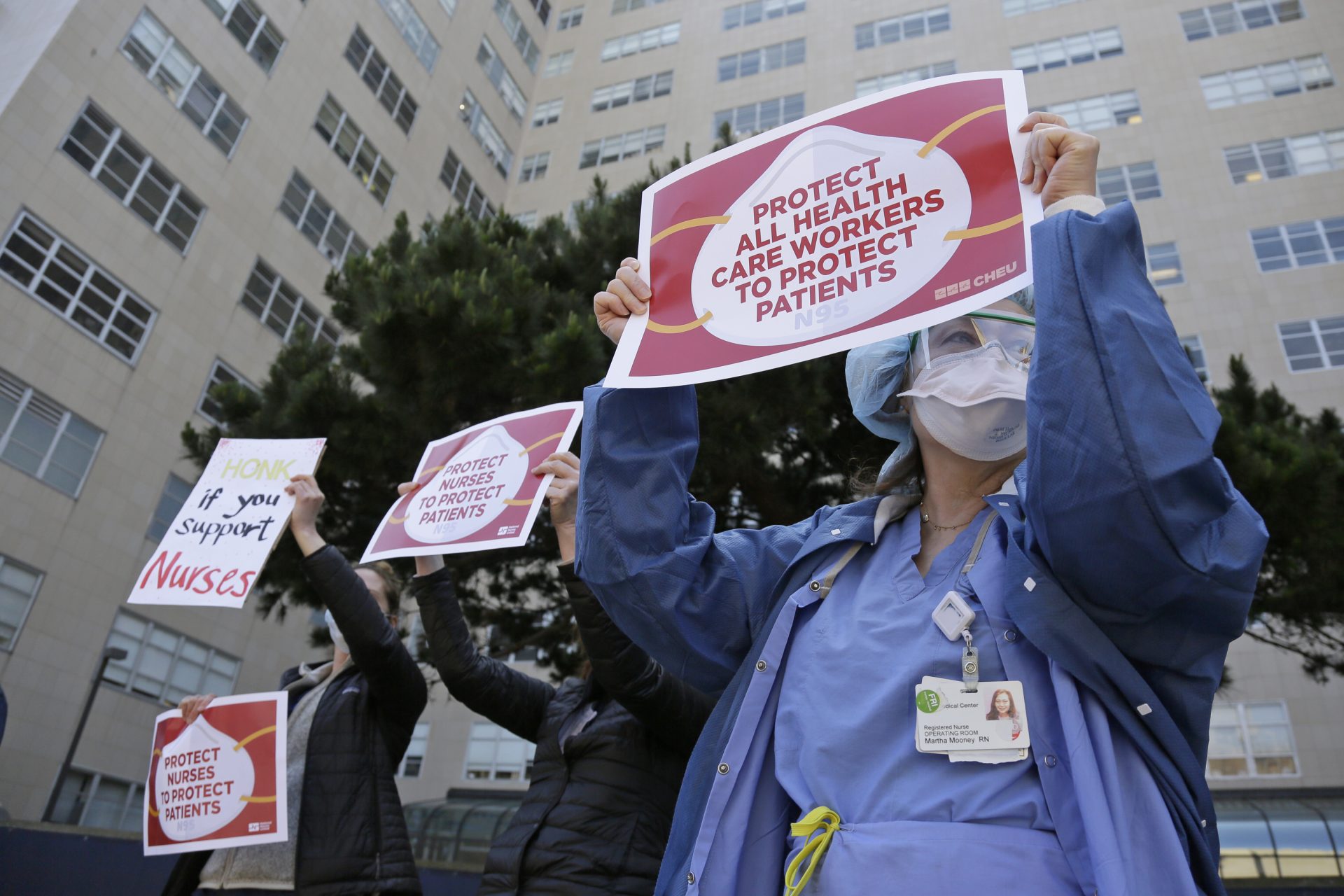 Operating room nurse Martha Mooney holds up a sign to honking motorists during a May Day action demanding better COVID-19 protections for health care workers outside the Parnassus campus of the UCSF Medical Center Friday, May 1, 2020, in San Francisco. The May Day actions by nurses were taking place at 139 hospitals in 13 states Friday.