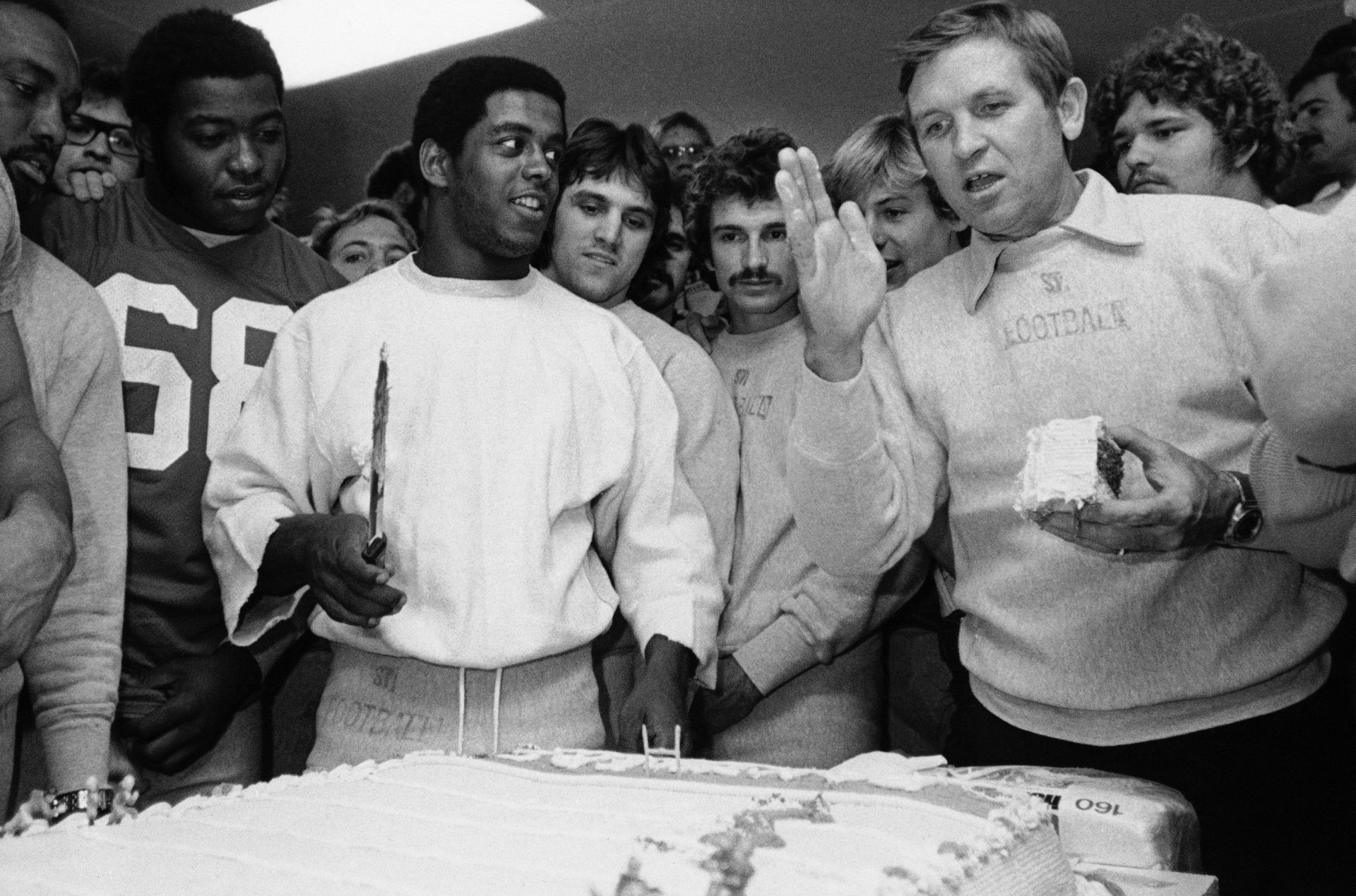 University of Pittsburgh running back Tony Dorsett, with knife, gets a little coaching about cake cutting by Pitt mentor Johnny Majors, right, before practice, Oct. 25, 1976 at Pitt Stadium in Pittsburgh. Dorsett, who broke the all-time NCAA rushing record on Saturday at Navy, was given a giant cake in the shape of a football field for his accomplishment by his teammate who surround him.