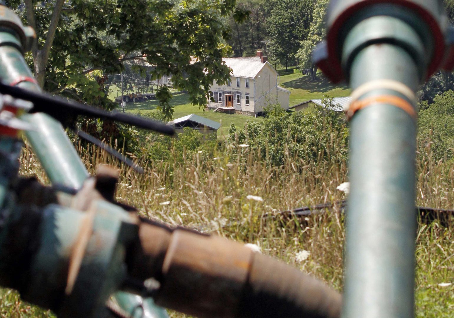 This July 27, 2011 file photo shows a farmhouse in the background framed by pipes connecting pumps where the hydraulic fracturing process in the Marcellus Shale was underway at a Range Resources site in Claysville, Pa. 