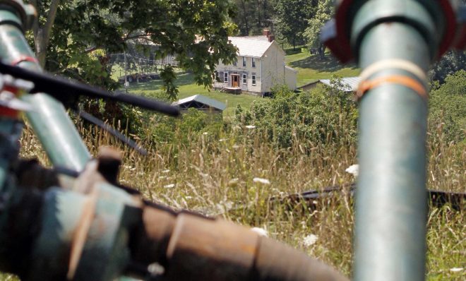 This July 27, 2011 file photo shows a farmhouse in the background framed by pipes connecting pumps where the hydraulic fracturing process in the Marcellus Shale was underway at a site in Claysville, Pa. 