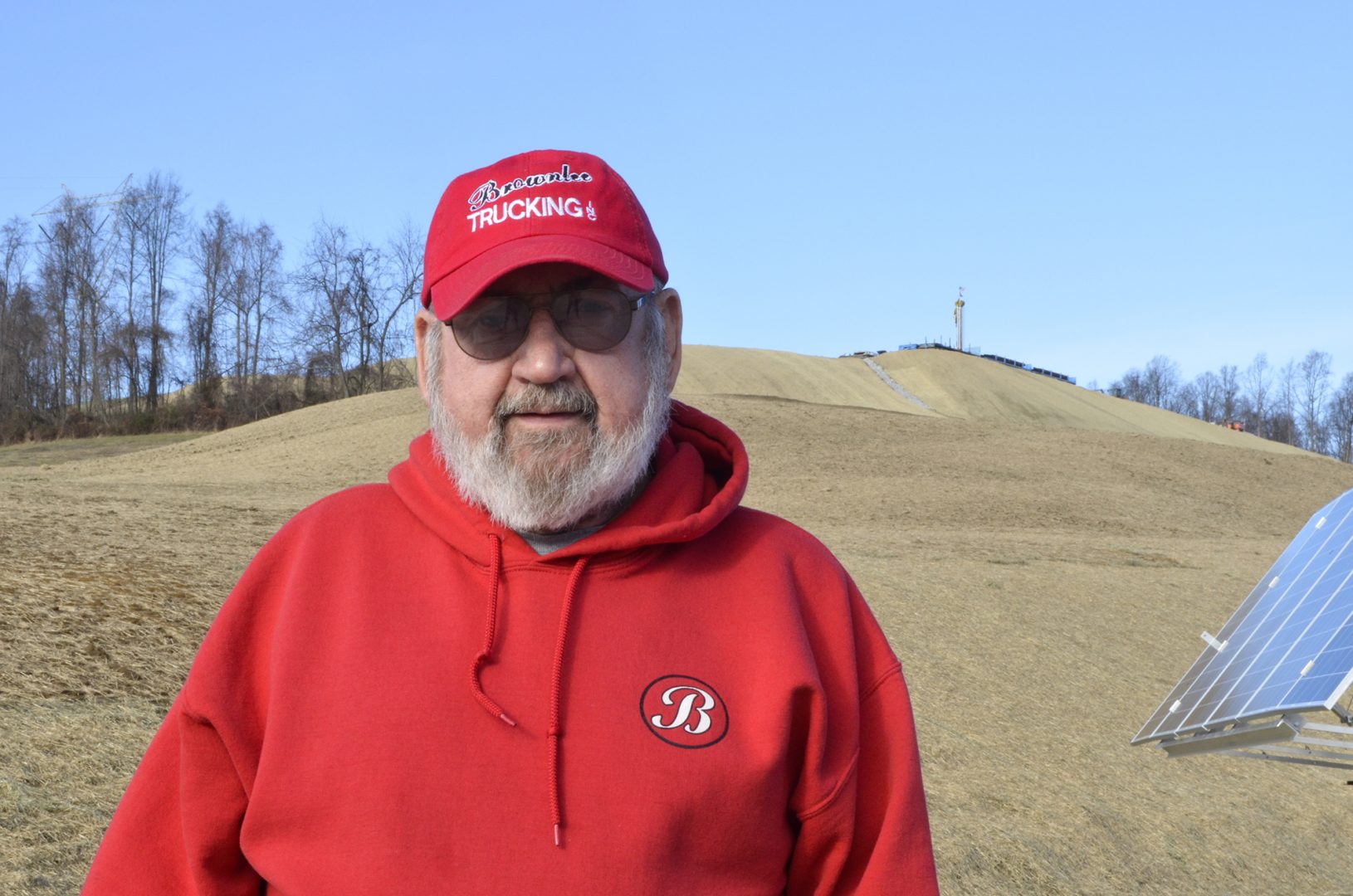 Washington County resident Frank Brownlee stands in his backyard, where a rig on the hill behind him is drilling natural gas wells.