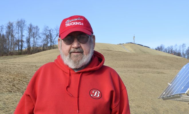 Washington County resident Frank Brownlee stands in his backyard, where a rig on the hill behind him is drilling natural gas wells.