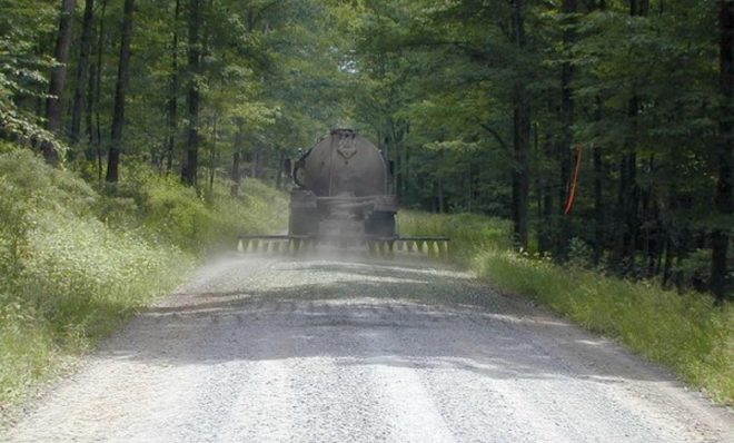 A truck sprays a dust suppressant on a dirt road in Pennsylvania. Some communities in Northwest Pennsylvania use conventional oil and gas waste as a suppressant. 