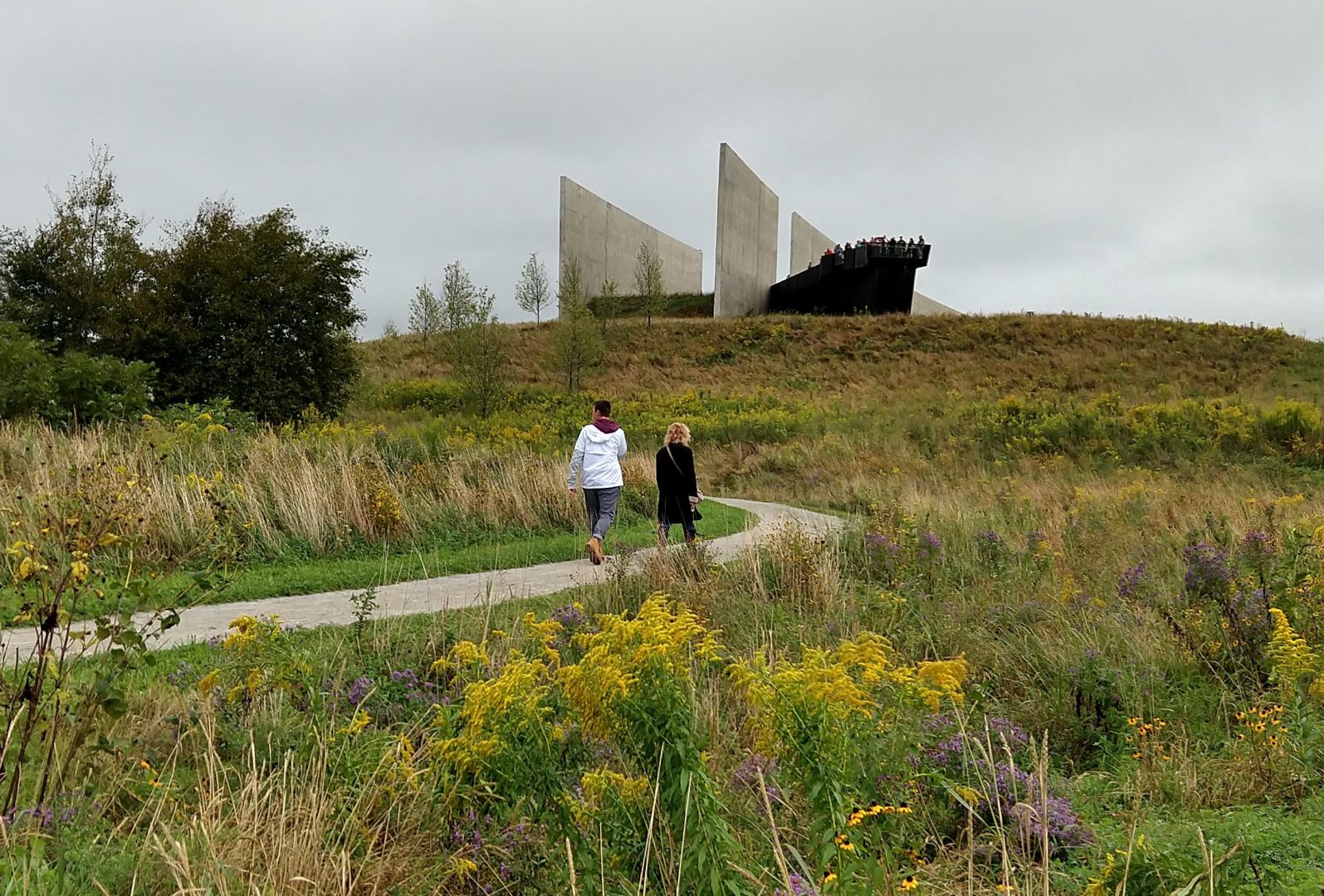 People walk along the path while a crowd gathers at the visitor's center overlook at the Flight 93 National Memorial on September 11, 2018. 