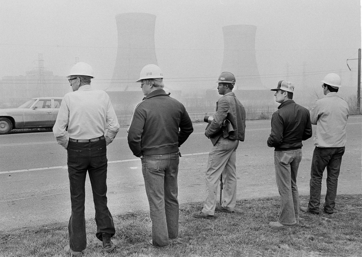 Workers from Metropolitan Edison's Three Mile Island nuclear plant stand outside visitors center early on March 30, 1979, as two cooling towers from the nuclear plant are visible in the background. Officials at the site declared an 