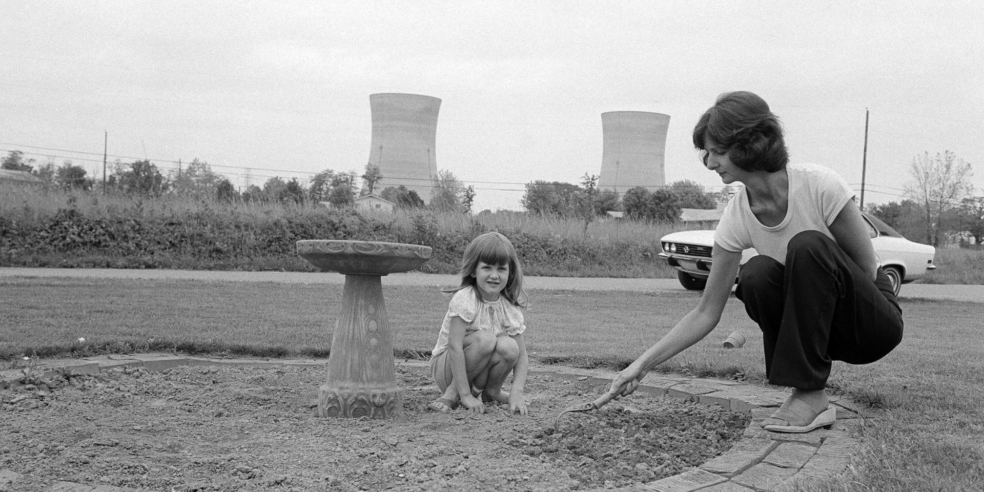 FILE PHOTO: Mrs. Joanne Noel, prepares her flower bed for planting in front of her Middletown, Pa., home as daughter Danielle, 4, watches as she sits on the ground, May 18, 1979. Noel evacuated her home with  her children during the crisis at Three Mile Island, seen in the background. 