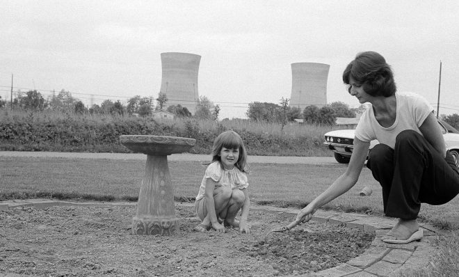 FILE PHOTO: Mrs. Joanne Noel, prepares her flower bed for planting in front of her Middletown, Pa., home as daughter Danielle, 4, watches as she sits on the ground, May 18, 1979. Noel evacuated her home with  her children during the crisis at Three Mile Island, seen in the background. 