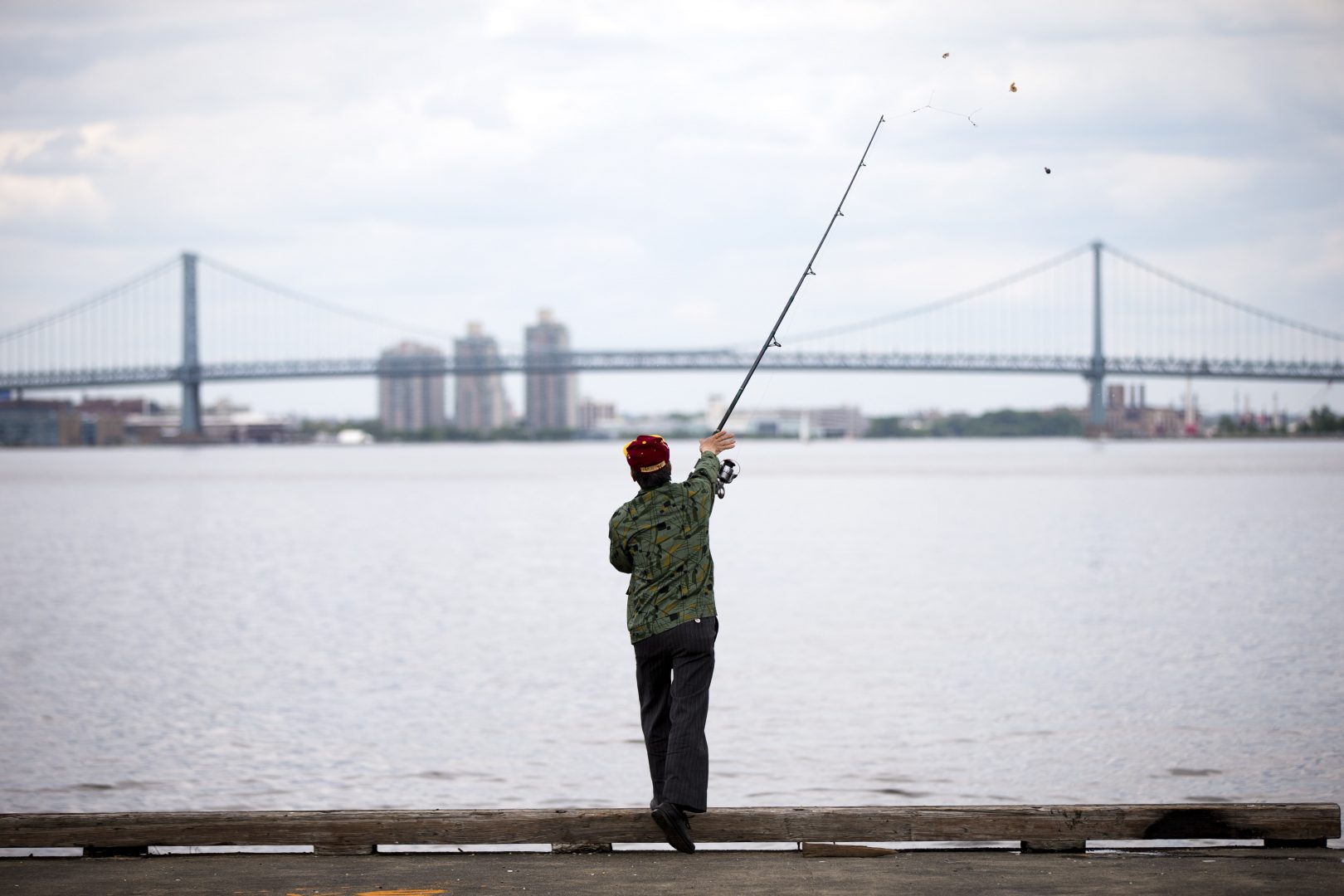 A man casts his line as he fishes for catfish in the Delaware River in view of the Benjamin Franklin Bridge. 