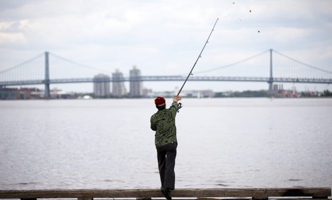 A man casts his line as he fishes for catfish in the Delaware River in view of the Benjamin Franklin Bridge. 