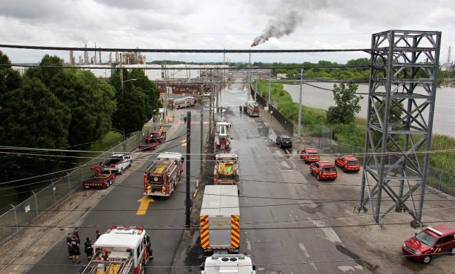 Philadelphia firefighters gather at the entrance to Philadelphia Energy Solutions Refinery, while a large flare burns off fuel to prevent it from feeding the massive fire at the refinery. 