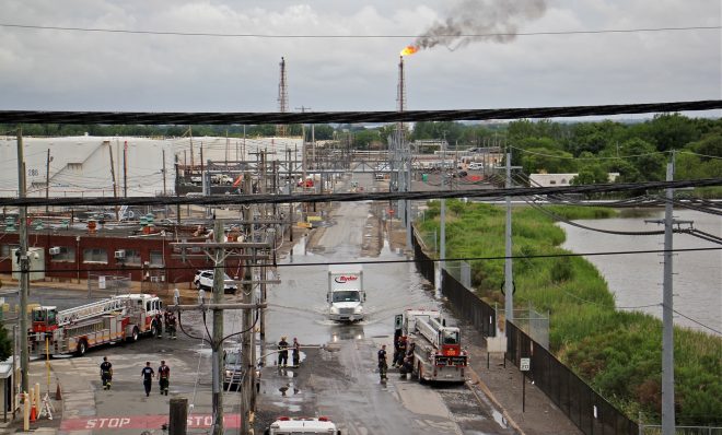 Philadelphia firefighters gather at the entrance to Philadelphia Energy Solutions Refinery, while a large flare burns off fuel to prevent it from feeding the massive fire at the refinery. (Emma Lee/WHYY)