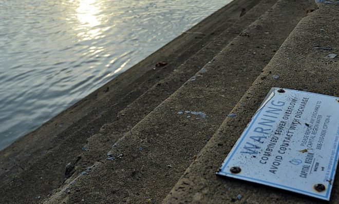 A Capital Region Water sign posted along the east bank of the Susquehanna River reads “Warning. Combined sewer overflow. Avoid contact with discharge.” 