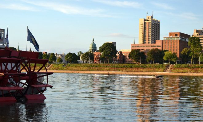 A man water-skis behind a boat on the Susquehanna River, as seen from City Island. In the foreground is the Pride of the Susquehanna boat. The state Capitol is visible across the river. 