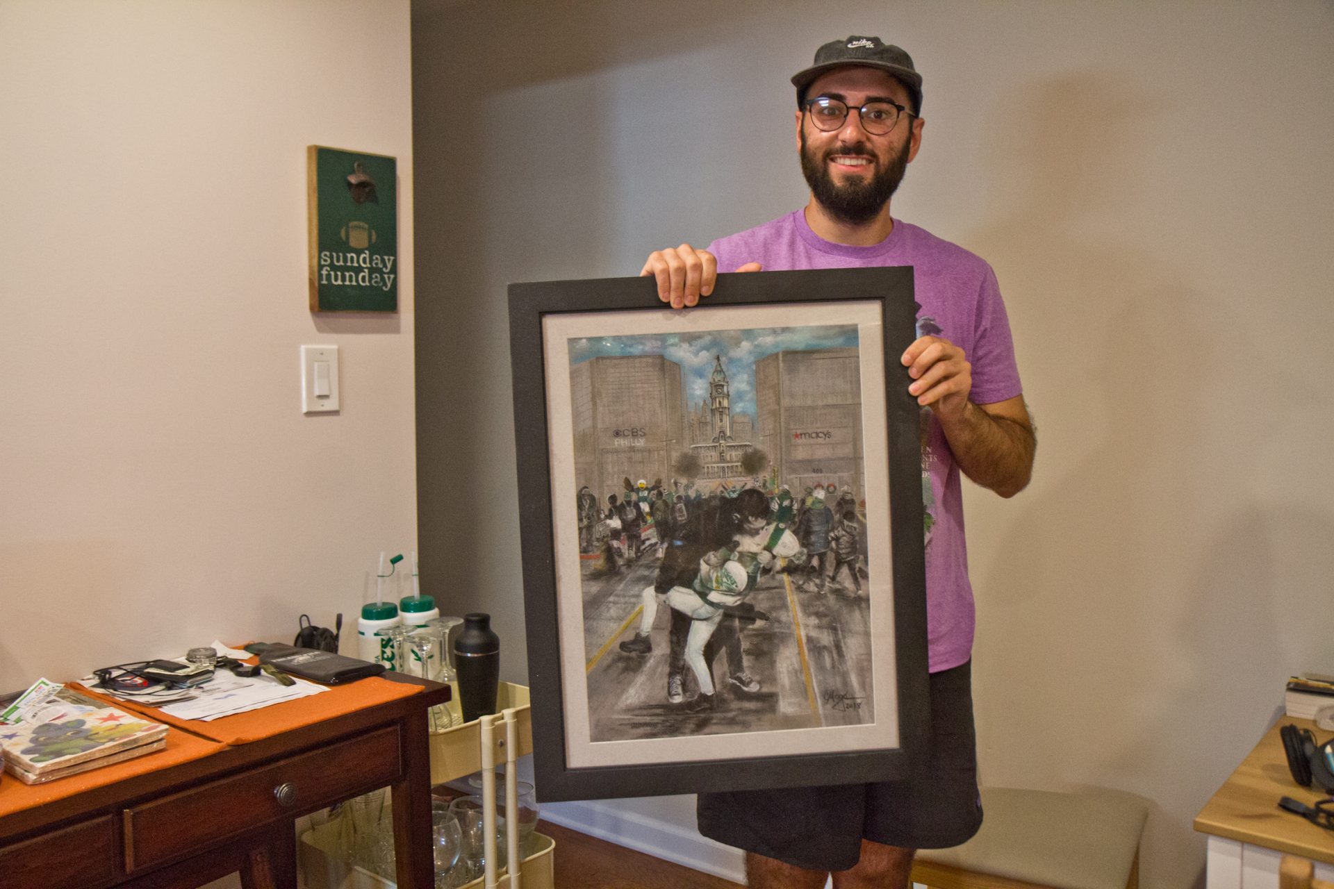 Shamus Clancy, a Philadelphia writer and sports super fan, holds a drawing recreation of a photo taken on the day of the Eagles Super Bowl parade, where a tweet set in motion the kiss that introduced Clancy to his girlfriend. 