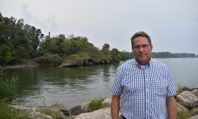 Mike Campbell, a college biology professor, is seen on Sept. 11, 2019, in a boat launch area with a smokestack of Erie Coke visible in the background.