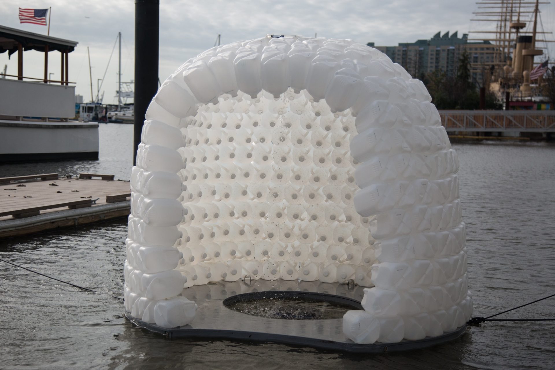Simone Spicer's Convergence sits in the river basin for the art exhibit FLOW. Plastic water jugs stand in for the ice blocks of an igloo that seems to be melting as it floats on the water.