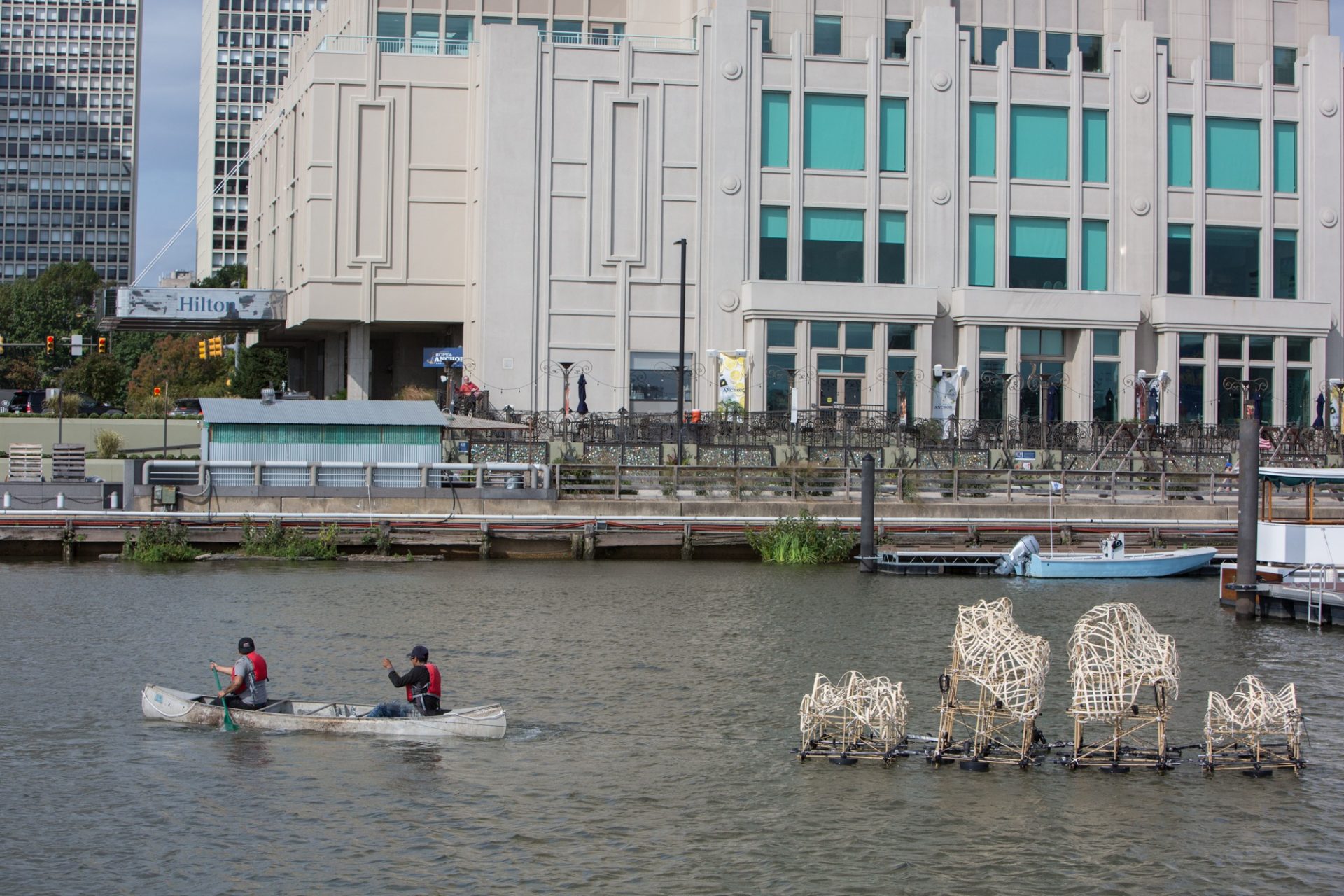 Two installers maneuver a canoe to steer Talasnik's sculpture into place.