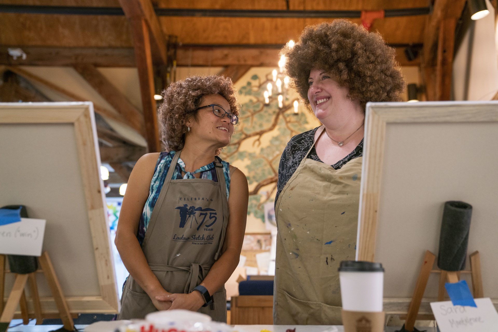 From left, Huyen MacMichael and Sara Monteleone exchange laughs during the  Bob Ross painting class at the Franklin Park Arts Center. MacMichael and Monteleone wore the iconic Bob Ross wig during the entire class.