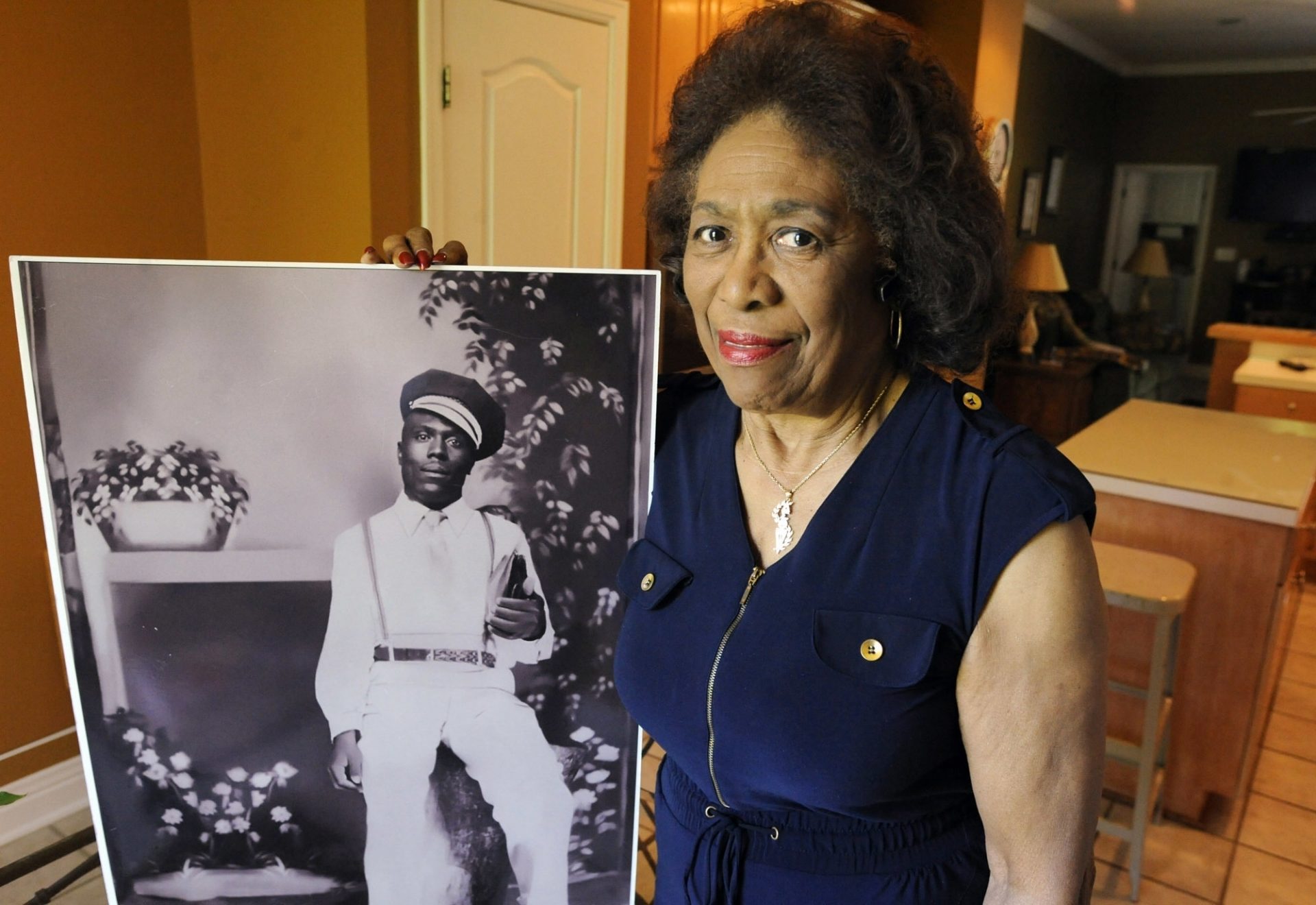 In this Wednesday, April 18, 2018 photo, Josephine Bolling McCall poses with a photo of her father, lynching victim Elmore Bolling, at her home in Montgomery, Ala.