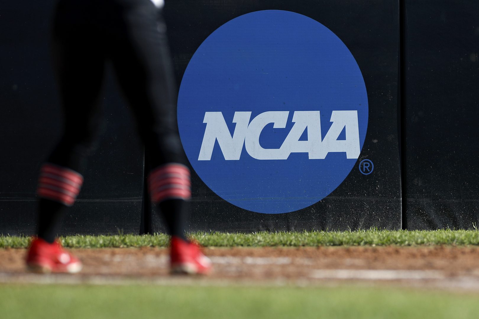 FILE PHOTO: In this April 19, 2019, file photo, an athlete stands near a NCAA logo during a softball game in Beaumont, Texas. The NCAA is poised to take a significant step toward allowing college athletes to earn money without violating amateurism rules. The Board of Governors will be briefed Tuesday, Oct. 29 by administrators who have been examining whether it would be feasible to allow college athletes to profit of their names, images and likenesses. A California law set to take effect in 2023 would make it illegal for NCAA schools in the state to prevent athletes from signing personal endorsement deals.