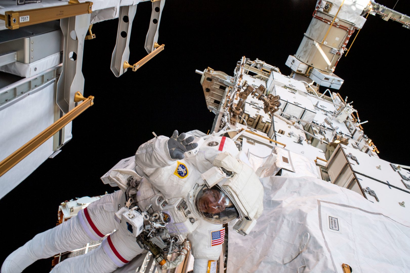 NASA astronaut Andrew Morgan waves to the camera while tethered on the Port 6 (P6) truss segment of the International Space Stations. He and fellow NASA astronaut Christina Koch (out of frame) worked to replace older hydrogen-nickel batteries with newer, more powerful lithium-ion batteries on the P6 truss during the six-hour and 45-minute spacewalk.