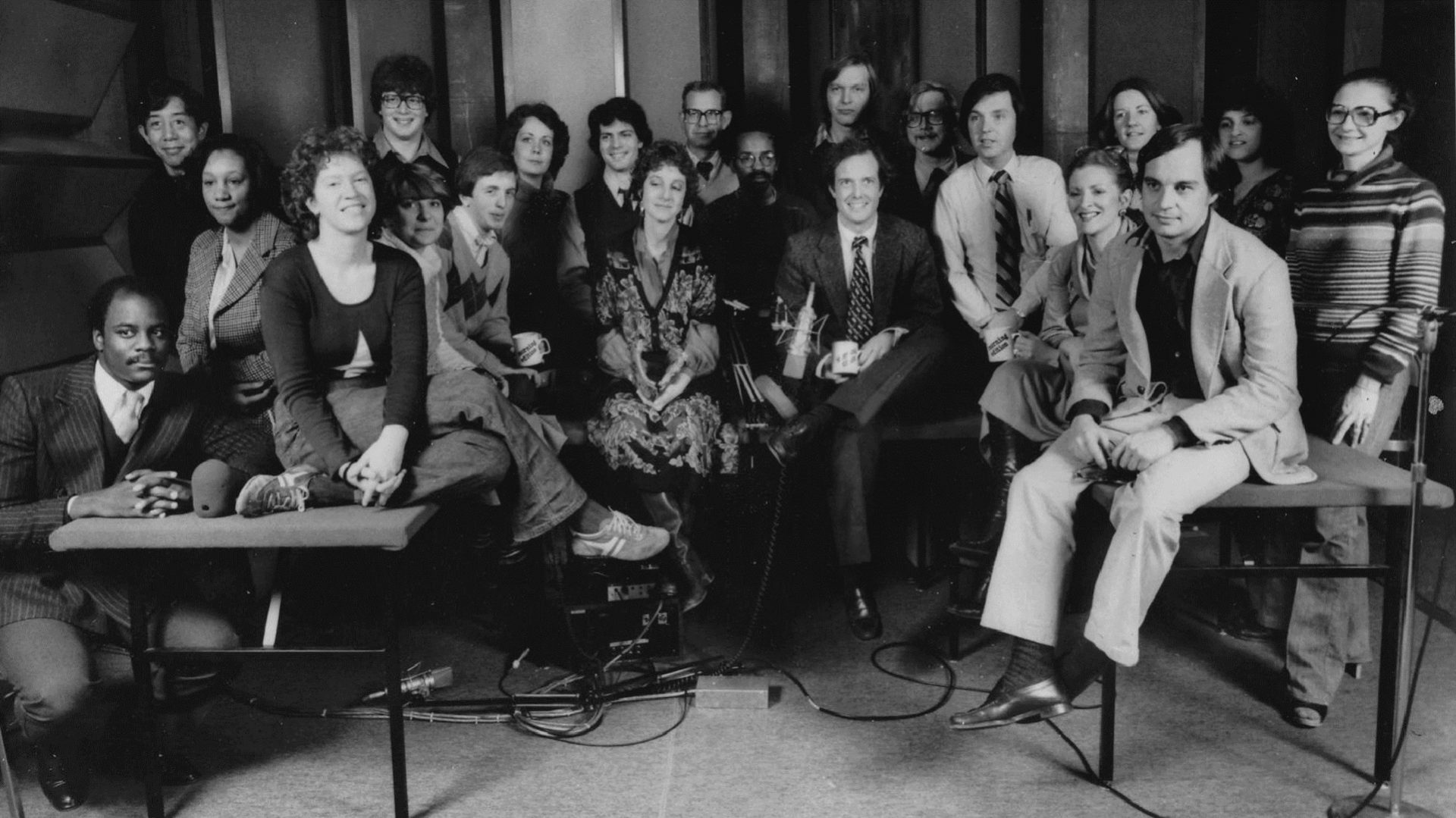 A staff photo taken during the early days of Morning Edition. Co-host Bob Edwards is in the back row, standing seventh from the left among the three men in glasses. His co-host, Barbara Hoctor, sits in the front, fourth from the left, between the two men holding mugs. Hoctor left the show after a few weeks. Edwards was host until 2004, when he went to SiriusXM.