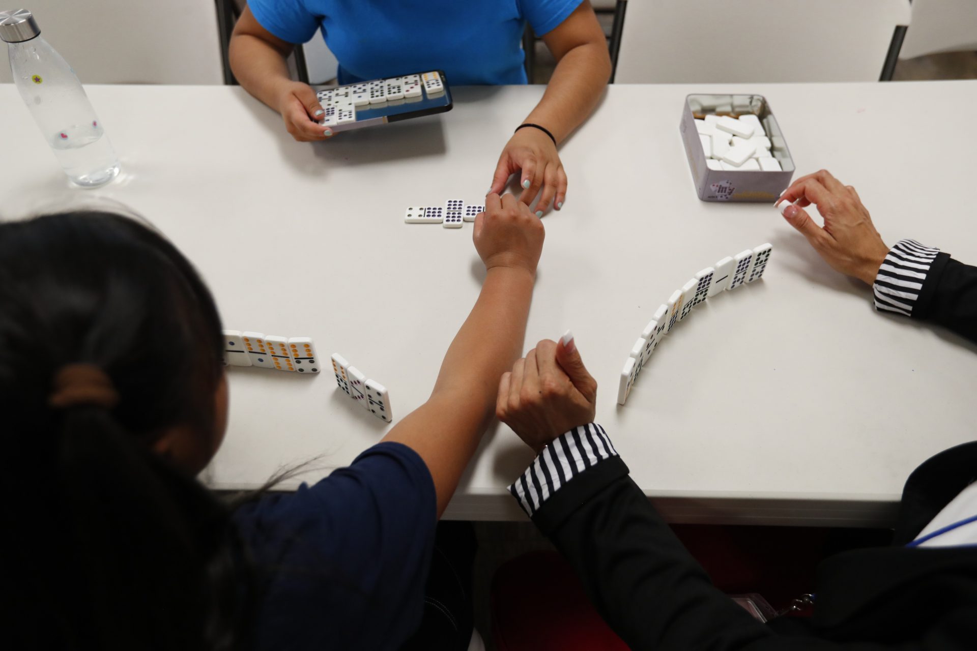 In this Sept. 24, 2019, photo, girls play dominos with a staff member at a shelter for migrant teenage girls, in Lake Worth, Fla. The nonprofit U.S. Committee for Refugees and Immigrants opened the federally funded Rinconcito del Sol shelter this summer, aiming to make it a model of excellence in a system of 170 detention centers, residential shelters and foster programs which held nearly 70,000 migrant kids in the past year.