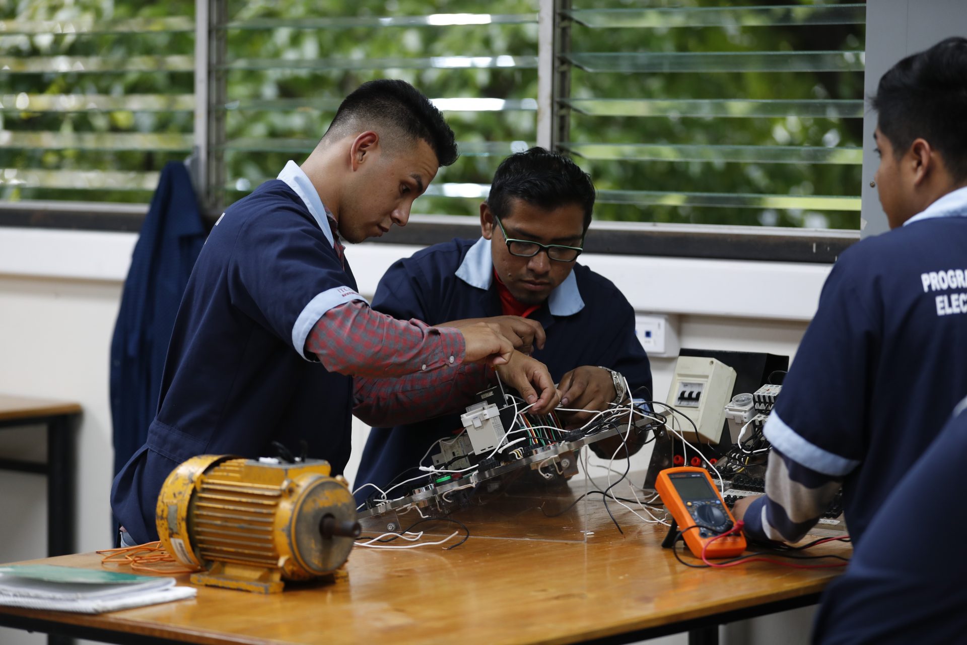 In this Oct. 11, 2019, photo, José Fernando Guillén Rodríguez, 21, left, practices building circuits with other students around a workbench in San Salvador, El Salvador. "I don't think about migrating anymore," said Guillén Rodríguez, 21, who was apprehended in the U.S. at 18 and spent time in adult detention before being deported. Now he's completed a year of daily electrical classes and works as an apprentice at an electrical construction company.