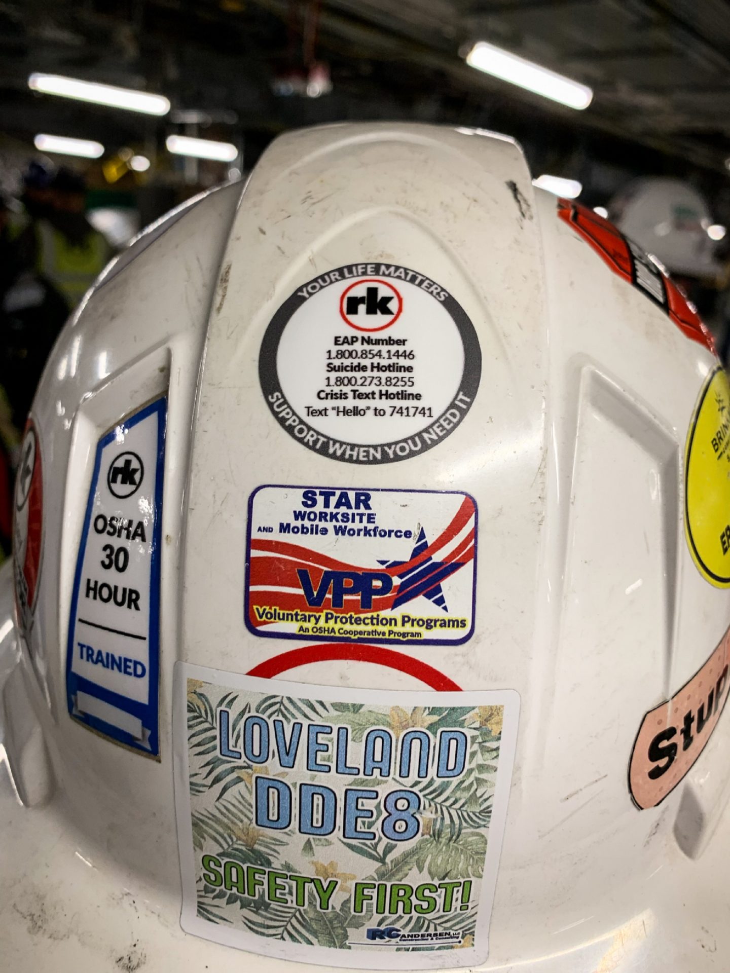 An RK hard hat sticker provides numbers for the company's employee assistance program, a suicide hotline and a crisis text line.