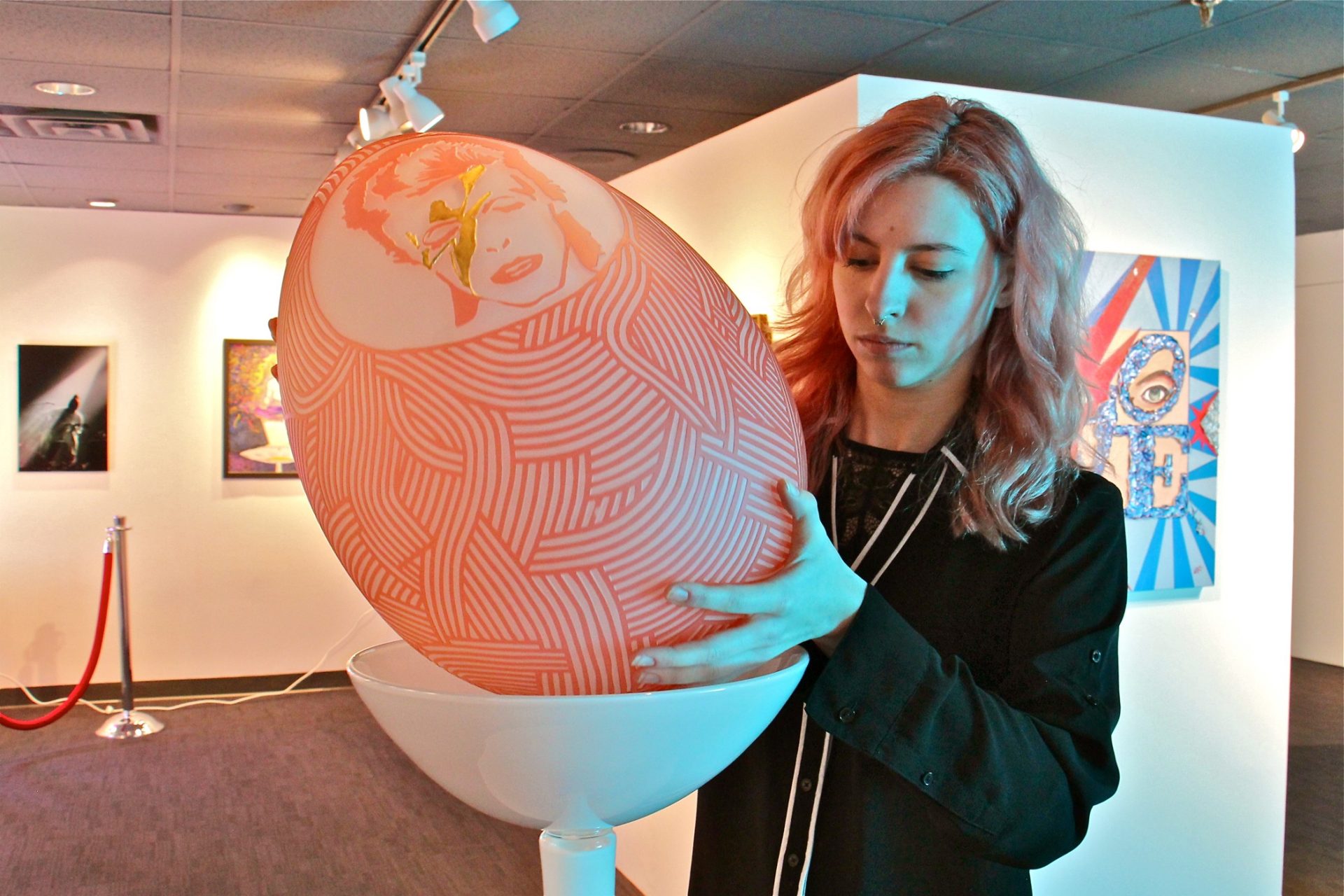 Curator Jocelyn Beaucher places Morgan Peterson's glass sculpture, 'Ziggy Stardust Modern Day Fabergé' part of the We Can Be Heroes exhibit at the Liberty Museum.