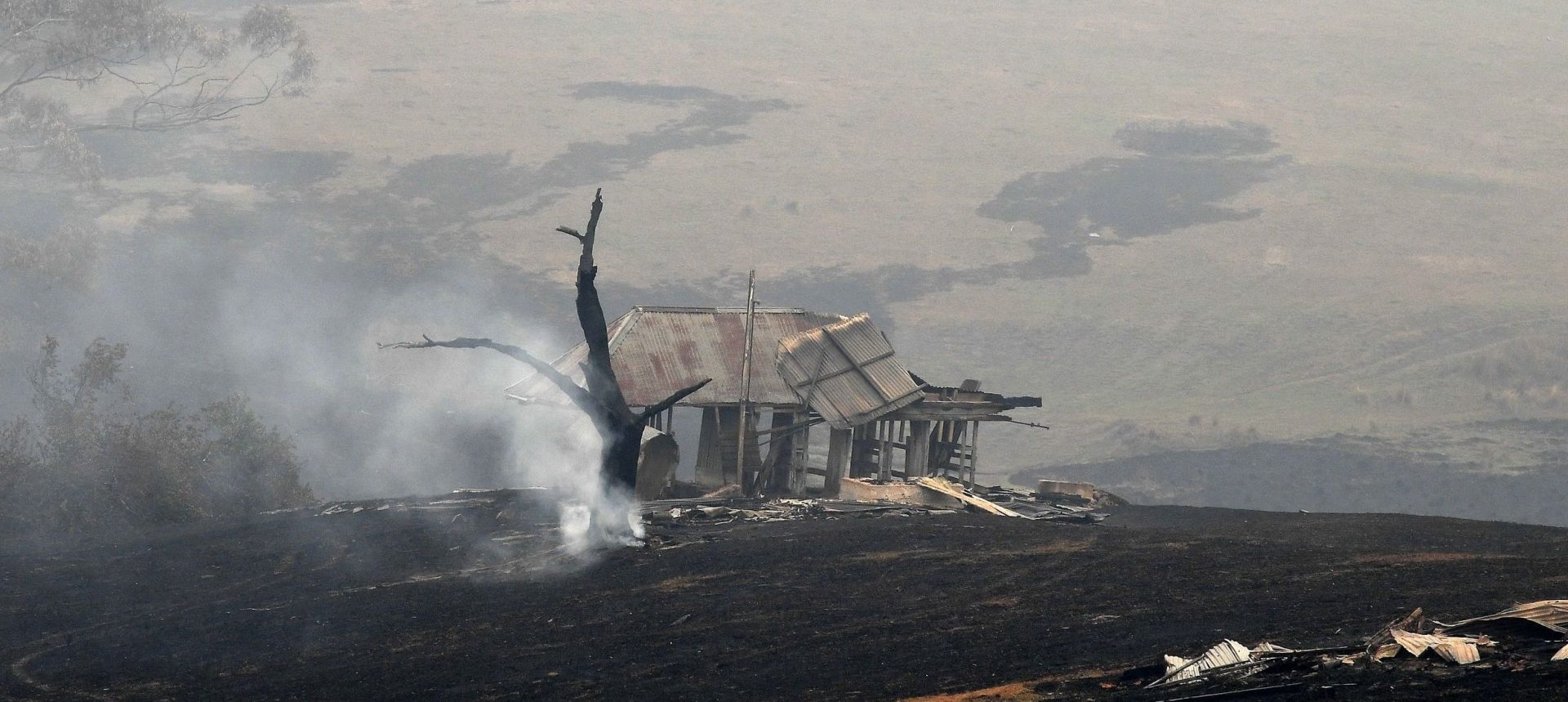 Smoke rises from a tree next to a fire-ravaged house in Australia's New South Wales on Monday. Reserve troops were deployed to parts of three Australian states after fires worsened over the weekend.