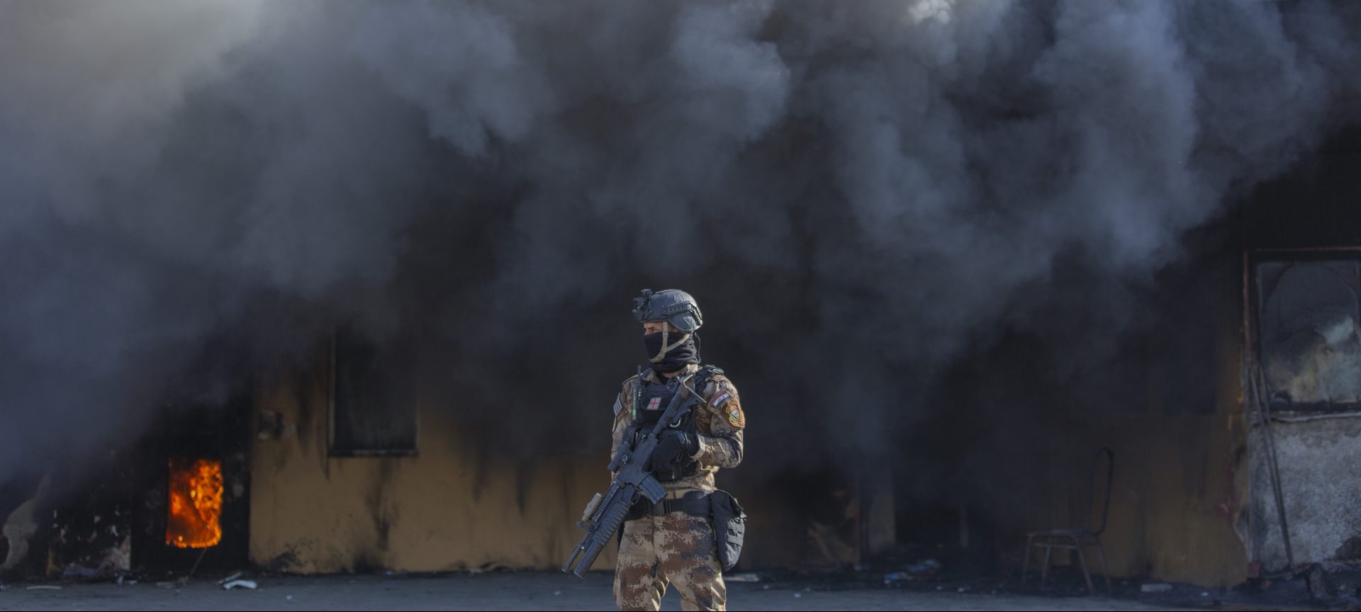 An Iraqi soldier stands guard in front of smoke rising from a fire set by pro-Iranian militiamen and their supporters in the U.S. embassy compound , in Baghdad, Iraq, Wednesday, Jan. 1, 2020. U.S. troops fired tear gas on Wednesday as hundreds of Iran-backed militiamen and other protesters gathered outside the American Embassy in Baghdad for a second day and set fire to the roof of a reception area inside the compound. 