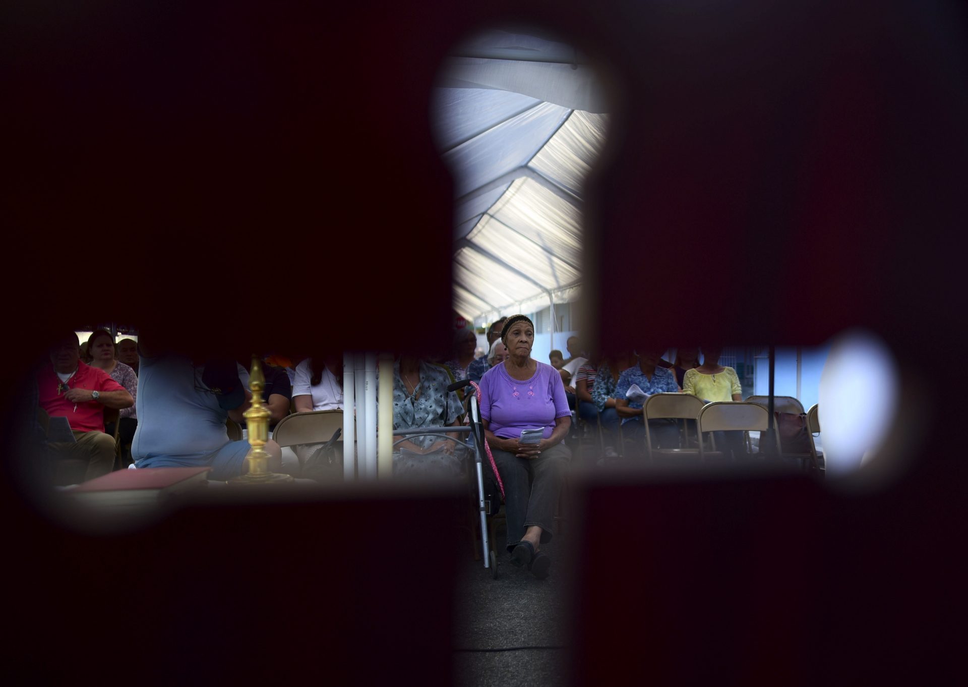 Seen through the cut-out shape of a cross on a priest's chair, a woman attends an outdoor Mass under a tent set up near the Immaculate Concepcion Catholic Church, which sustained earthquake-related damaged earlier in the week, following a magnitude 5.9 quake earlier in the day in Guanica, Puerto Rico, Saturday, Jan. 11, 2020. The morning quake caused further damage along the islandâ€™s southern coast, where previous recent quakes have toppled homes and schools.