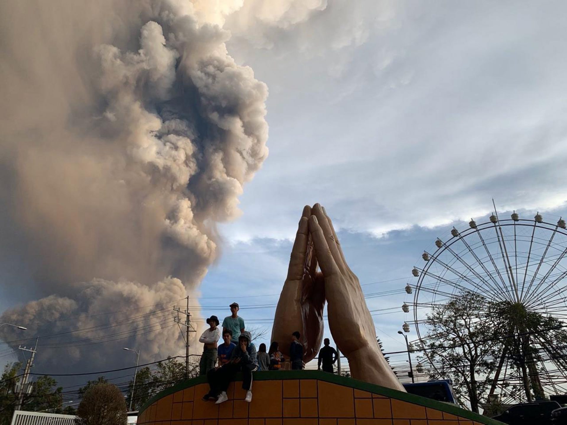 People watch as the Taal volcano spews ash and smoke during an eruption in Tagaytay, Cavite province south of Manila, Philippines on Sunday. Jan. 12, 2020. A tiny volcano near the Philippine capital that draws many tourists for its picturesque setting in a lake belched steam, ash and rocks in a huge plume Sunday, prompting thousands of residents to flee and officials to temporarily suspend flights.