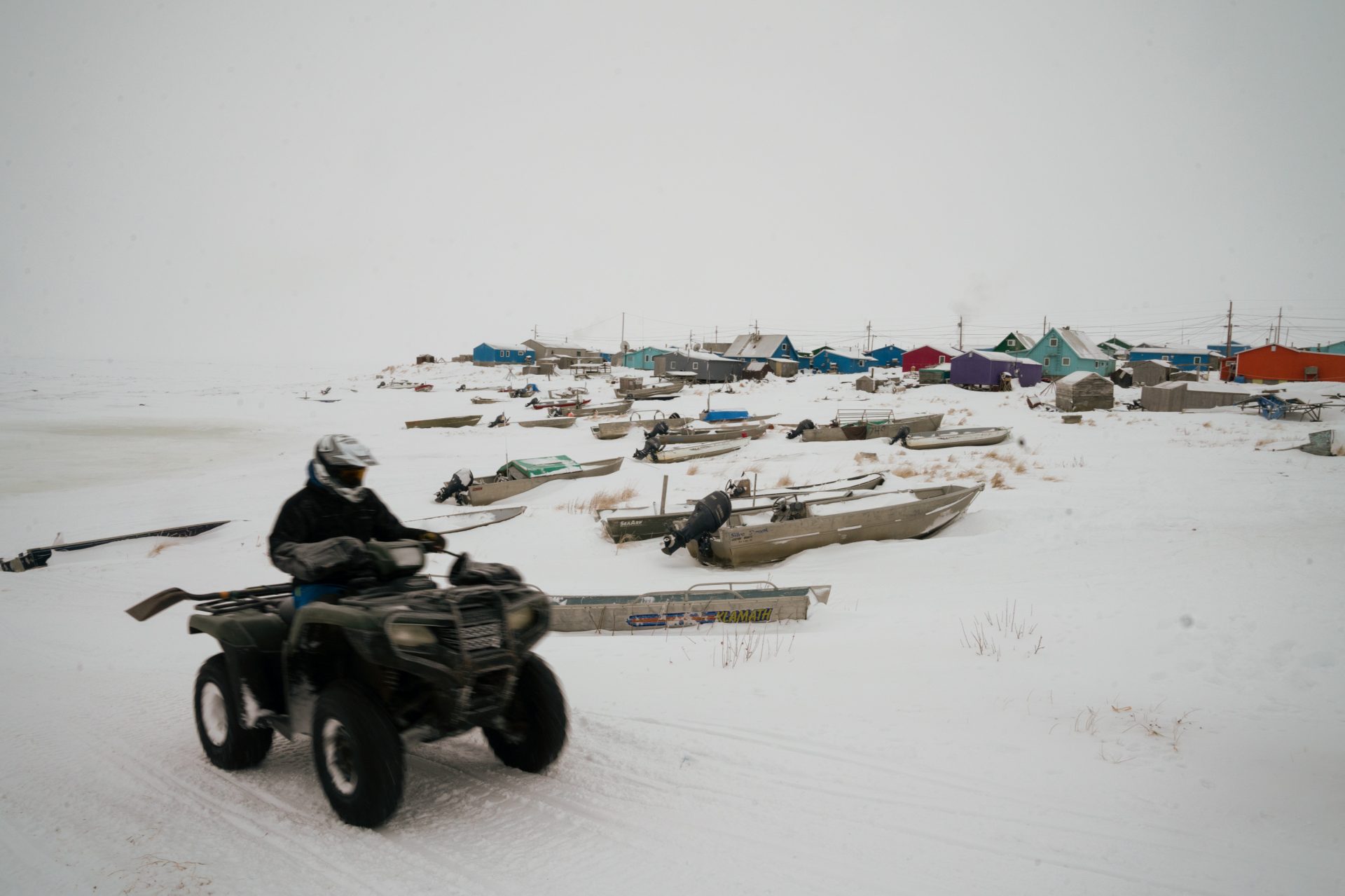 A person on an all-terrain vehicle drives past boats at the edge of Toksook Bay. During winter, census workers are able to journey across miles of frozen ground and ice roads to reach villages usually accessible only by plane or boat in the warmer months.