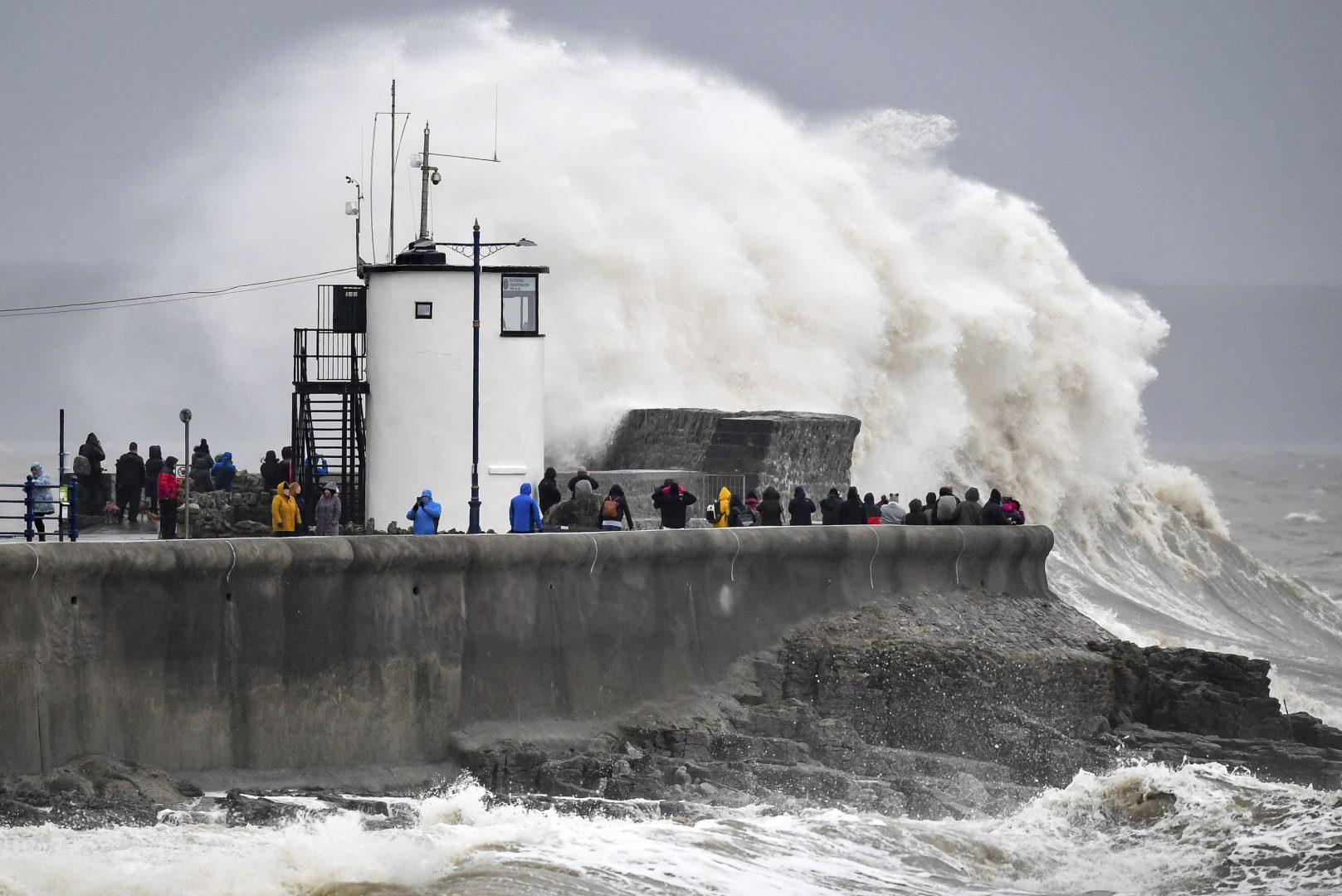 People watch waves and rough seas pound against the harbour wall at Porthcawl in Wales, as Storm Dennis sweeps across the country, Saturday Feb. 15, 2020.  Enormous waves  are churning across the North Atlantic as Britain braces for a second straight weekend of wild winter weather and flooding. (Ben Birchall/PA via AP)