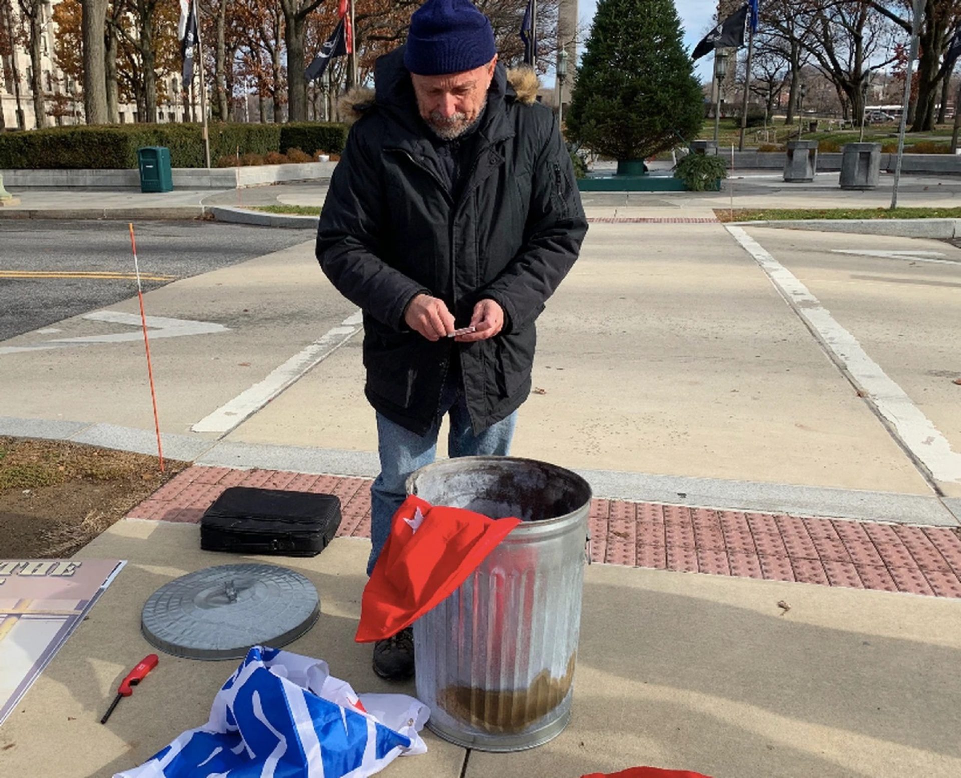 Citizen activist Gene Stilp prepares to strike a match to set one of his Trump campaign flags on fire outside the Pa. Capitol on Dec. 5, 2019. On Tuesday, a Harrisburg district judge found him not guilty of violating a city burn ban.