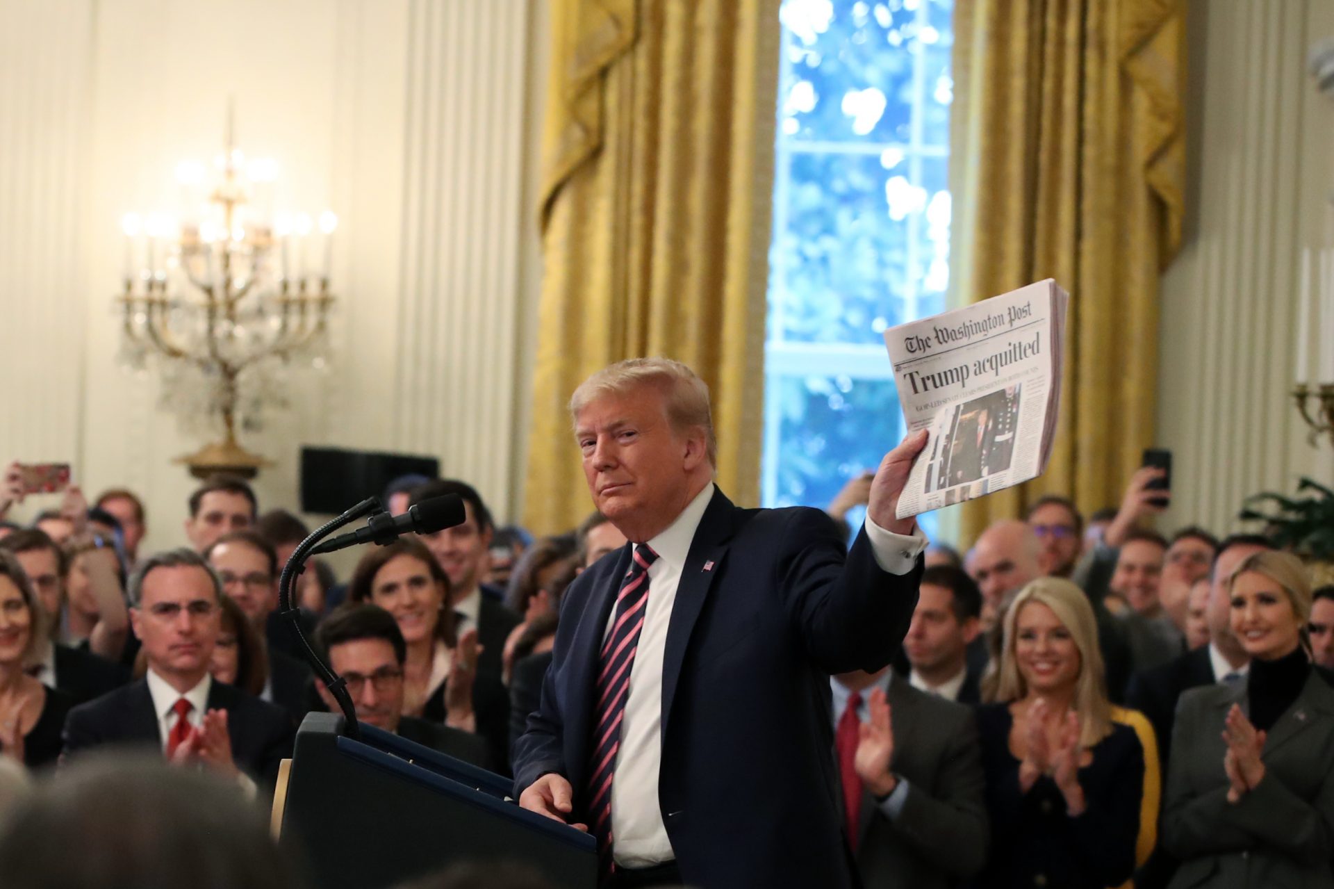 President Trump, surrounded by members of his administration and supporters, holds up a newspaper during remarks at the White House on Thursday.