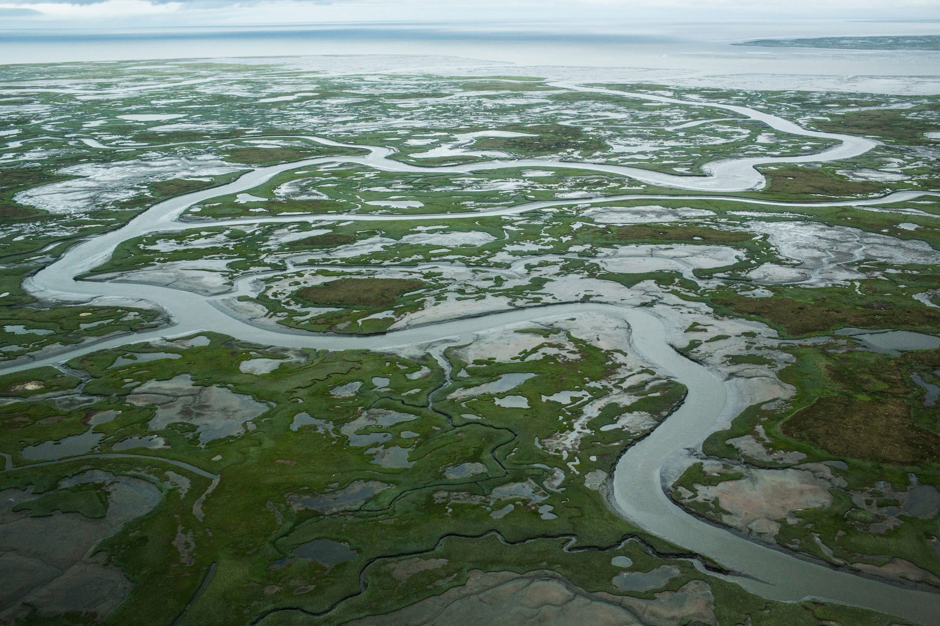 A marshy tundra landscape surrounds Newtok in the warmer months. The increased melting of sea ice is causing the Ninglick River to widen, eroding the riverbank. Larger storms that come in from the Bering Sea further erode the land.