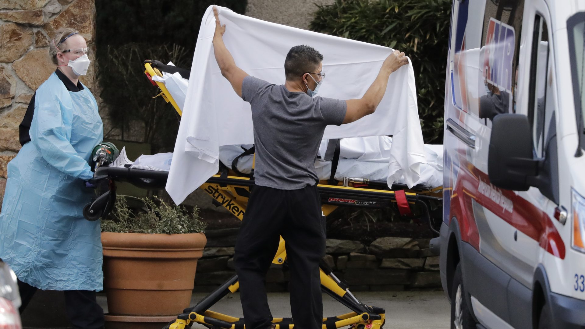 A staff member holds a sheet as a privacy screen as a person on a stretcher is taken to an ambulance from Life Care, a nursing facility where dozens of people are being tested for the COVID-19 virus in Kirkland, Wash., northeast of Seattle.