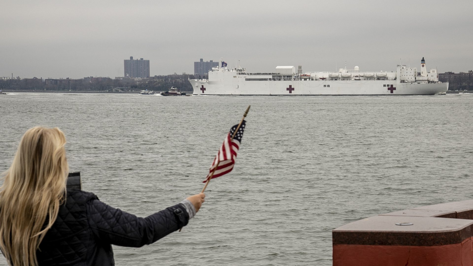 The U.S. Navy hospital ship Comfort is welcomed to New York City by Charlene Nickloan, waving a flag from the Matthew Buono war memorial in Staten Island, N.Y., on Monday.