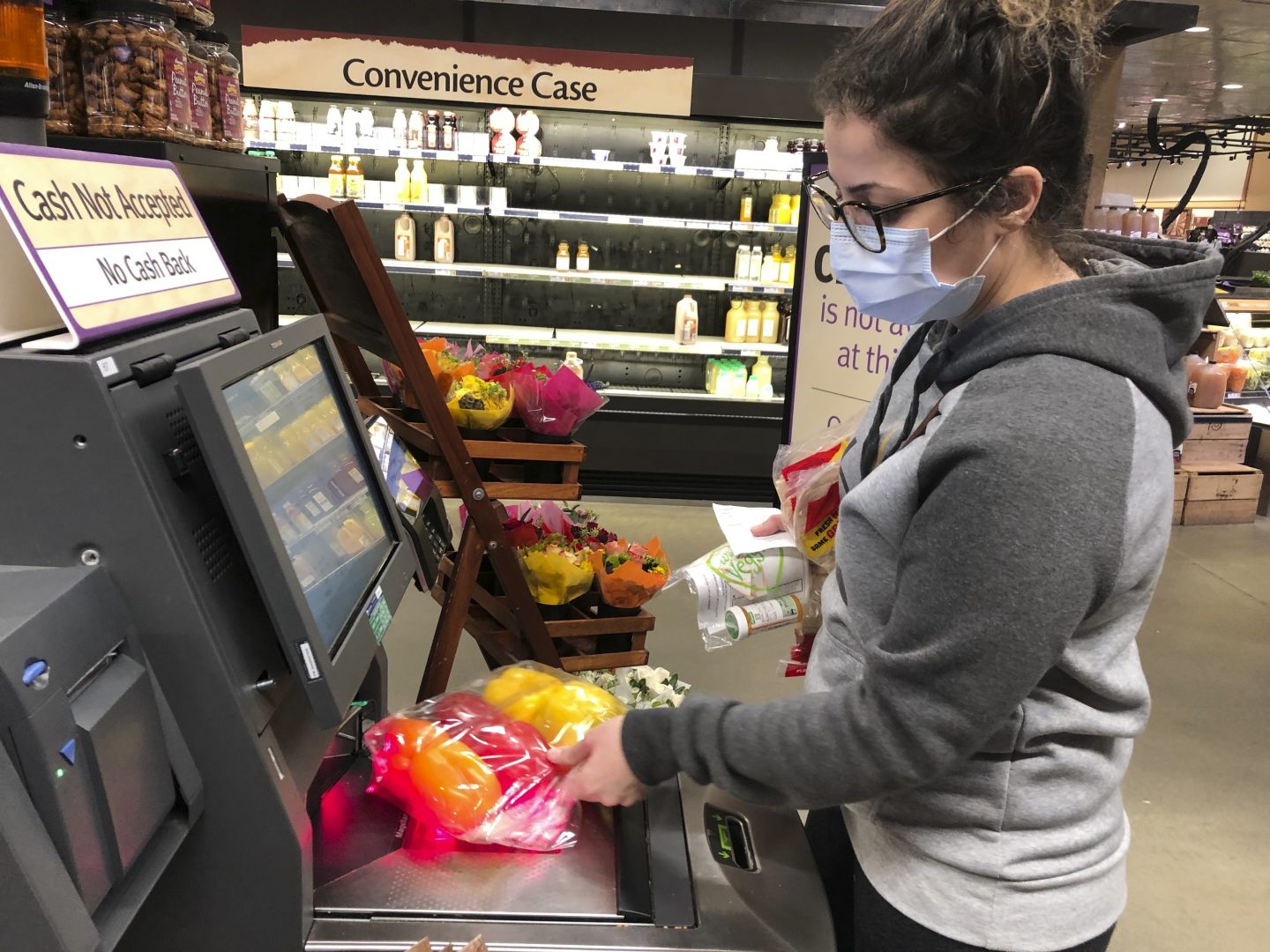 Wearing a surgical mask, Melissa Hall checks out of a Wegmans supermarket, Friday, March 13, 2020 in King of Prussia, Pa.,  Gov. Tom Wolf ordered schools, community centers, gyms and other venues in Montgomery County, a Philadelphia suburb, to shut down for two weeks amid a concentration of novel coronavirus cases there. (AP Photo/Michael Rubinkam)
