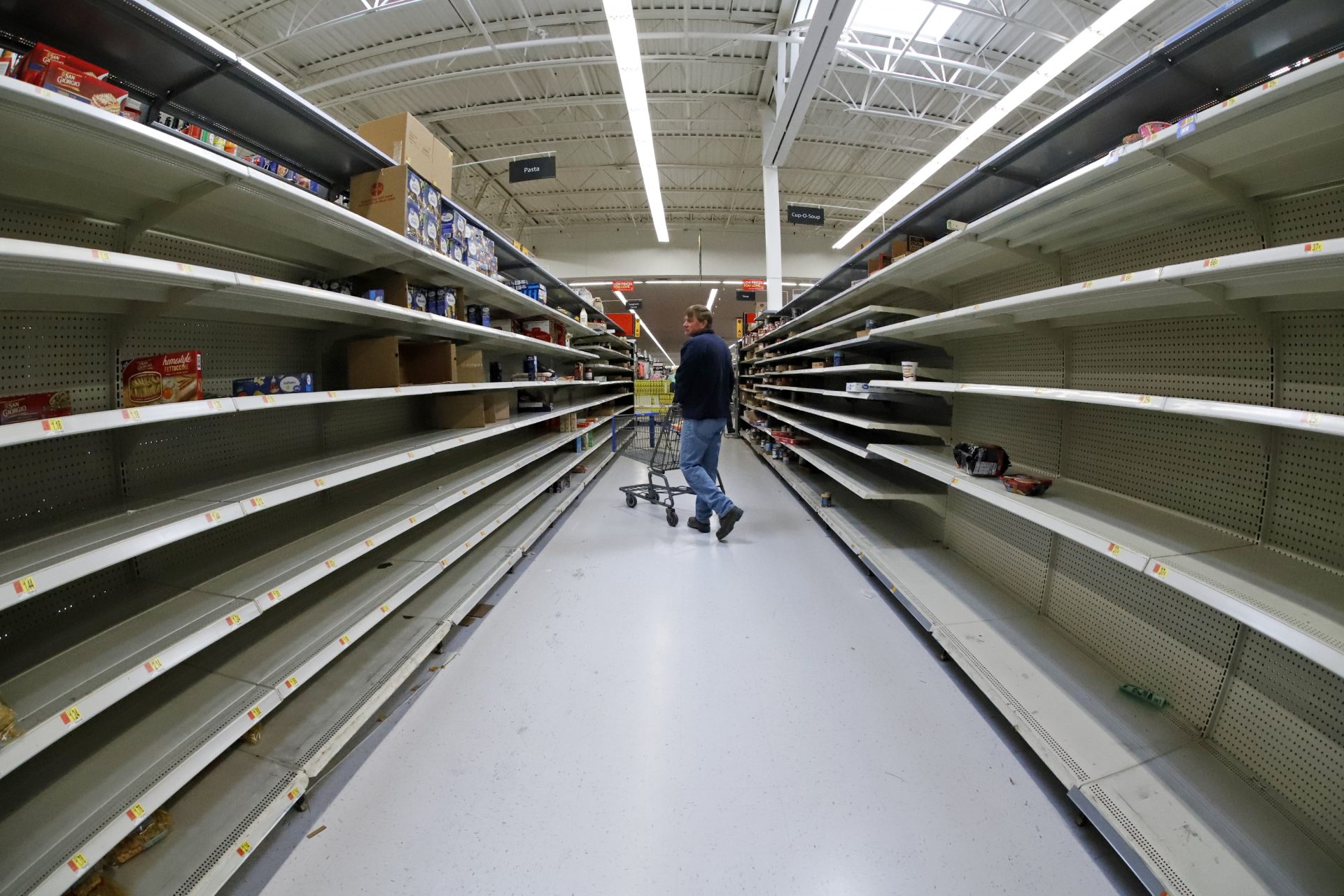 A man shops in an aisle of mostly empty shelves in a Walmart in Cranberry Township, Pa., Friday, March 13, 2020.