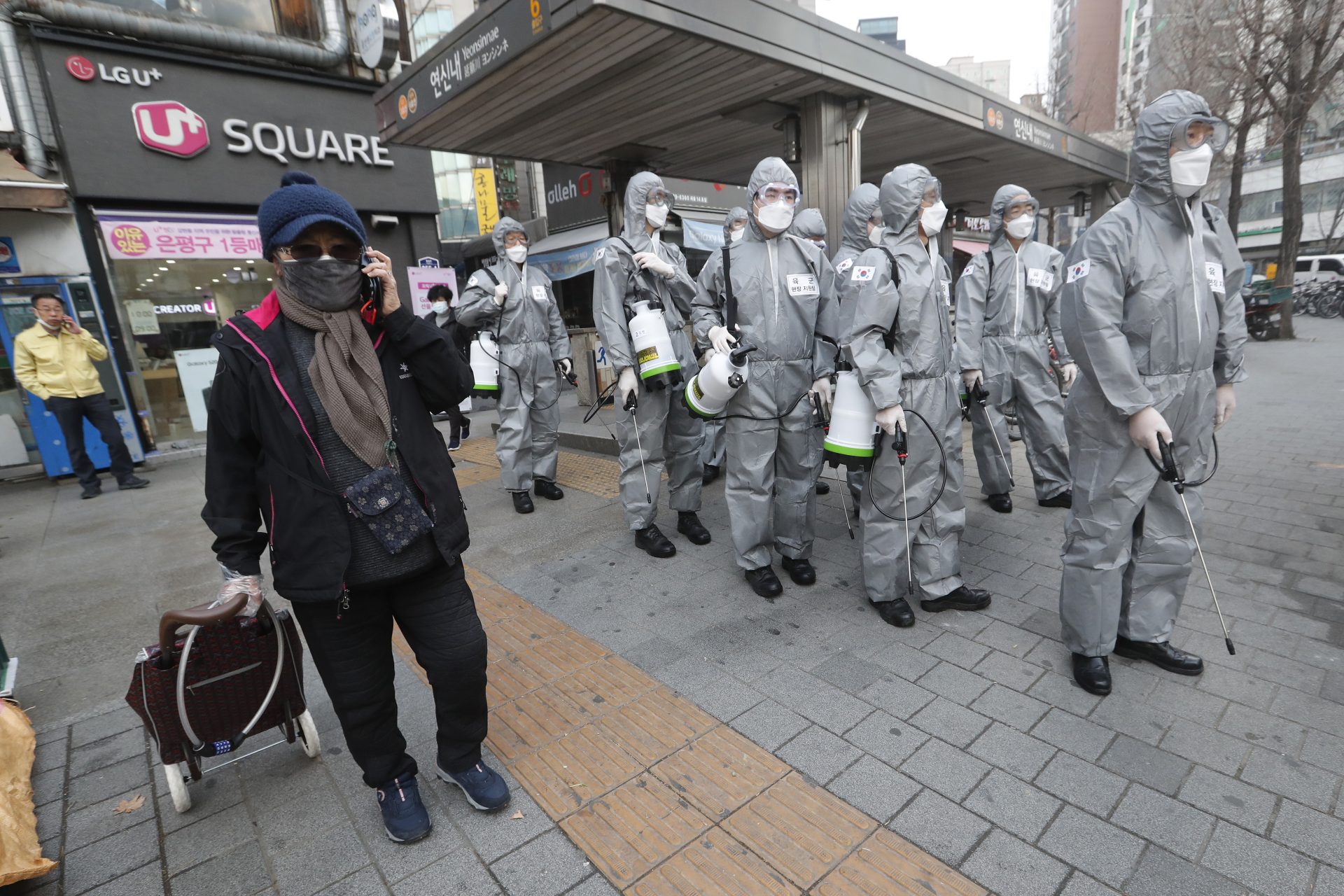 A woman passes by South Korean army soldiers wearing protective gears as they stand to spray disinfectant as a precaution against the new coronavirus at a shopping street in Seoul, South Korea, Wednesday, March 4, 2020. The coronavirus epidemic shifted increasingly westward toward the Middle East, Europe and the United States on Tuesday, with governments taking emergency steps to ease shortages of masks and other supplies for front-line doctors and nurses.